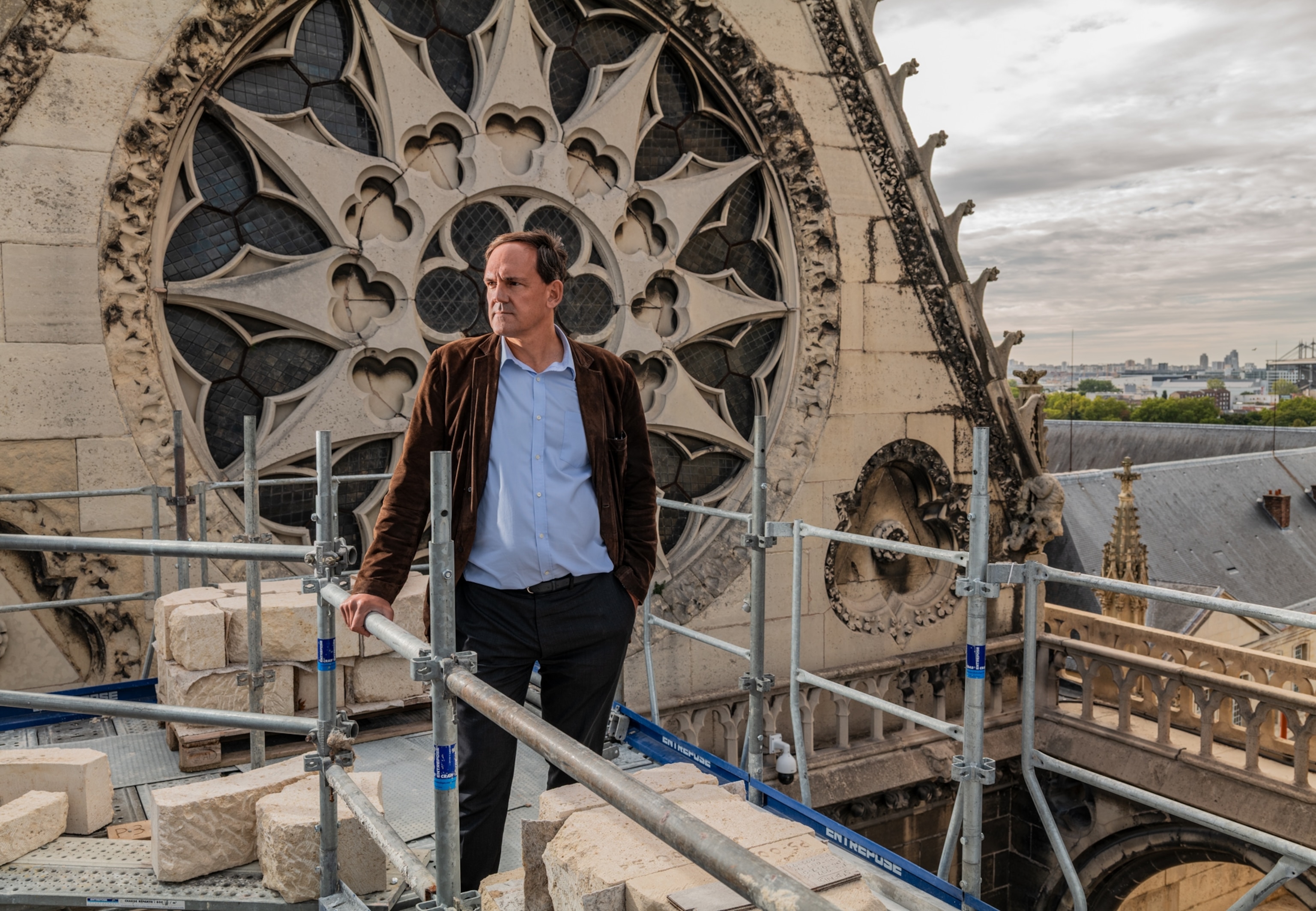 Man in blue shirt and brown velvet jacket on the scaffolds by the Rose Window of the cathedral.