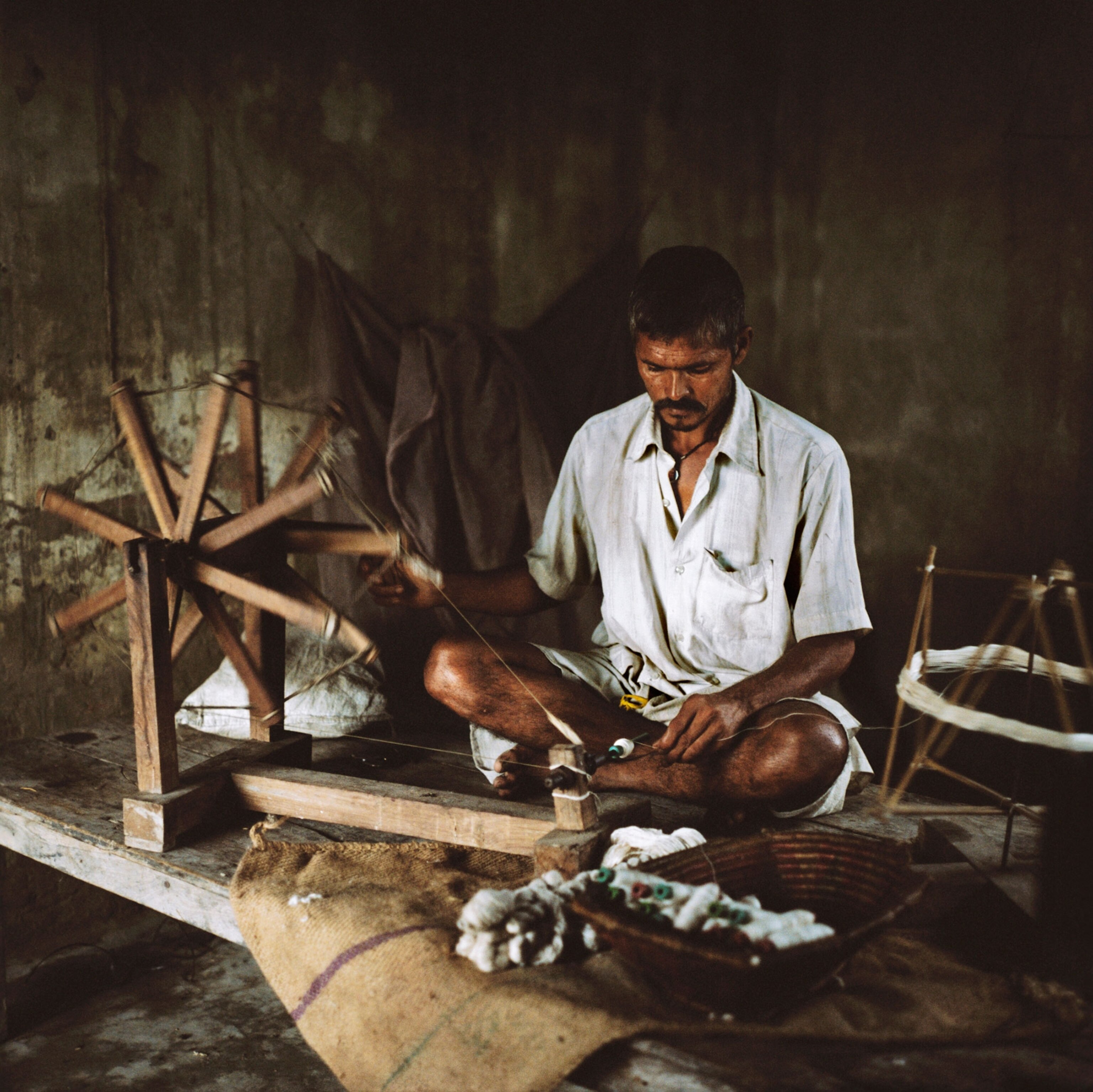 a man spinning cotton on a traditional  wheel or charkha while sitting on the floor in his home in Bihar