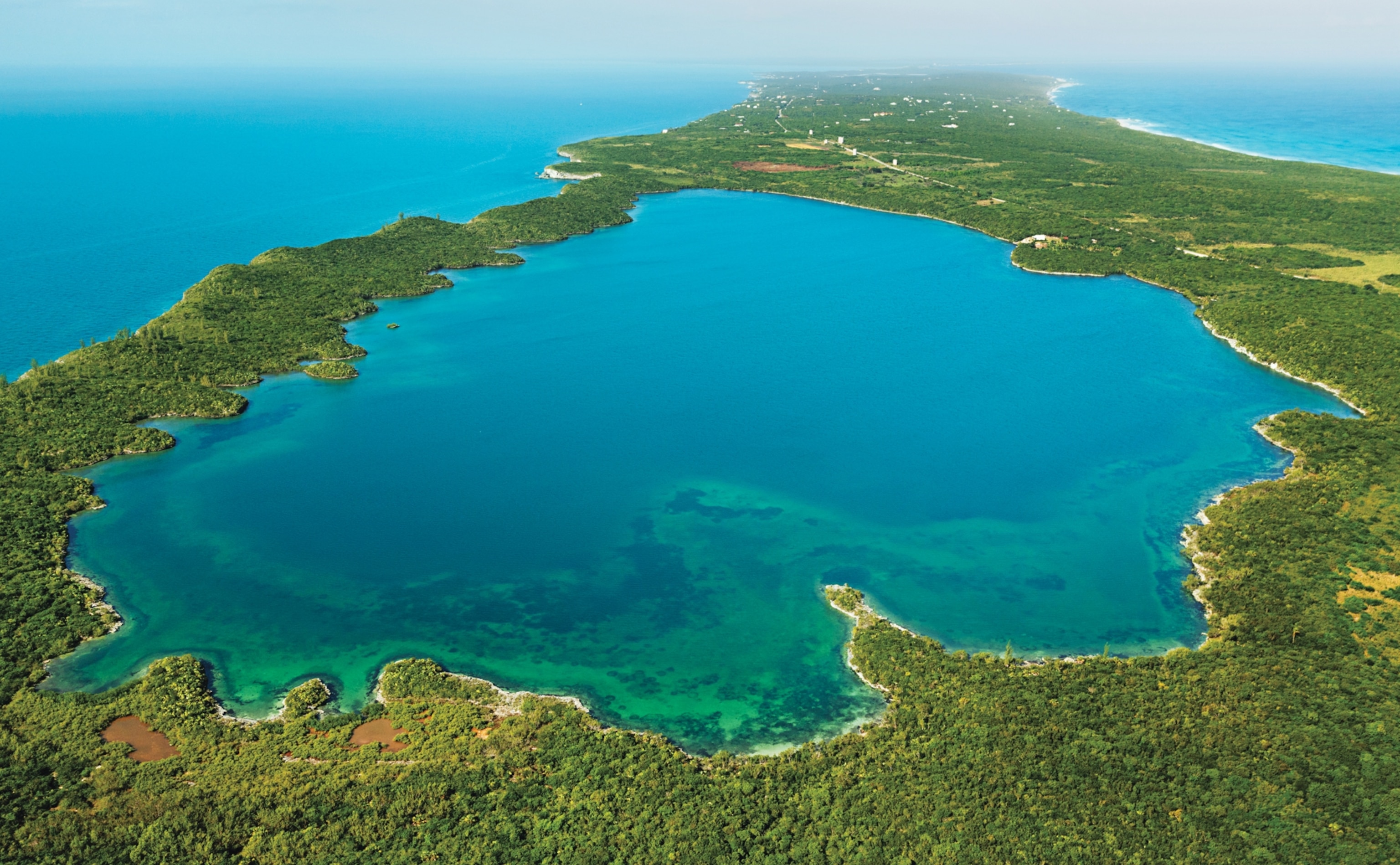 Aerial view of blue water pond separated from the ocean waters by narrow strip of green land.