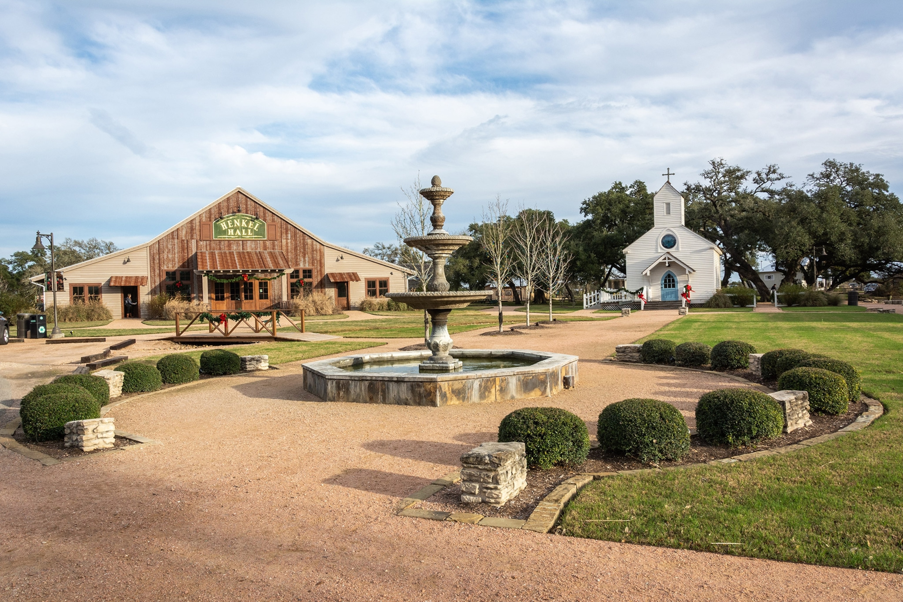 An outdoor square surrounded by a barn, a white church, and manicured lawn and shrubs
