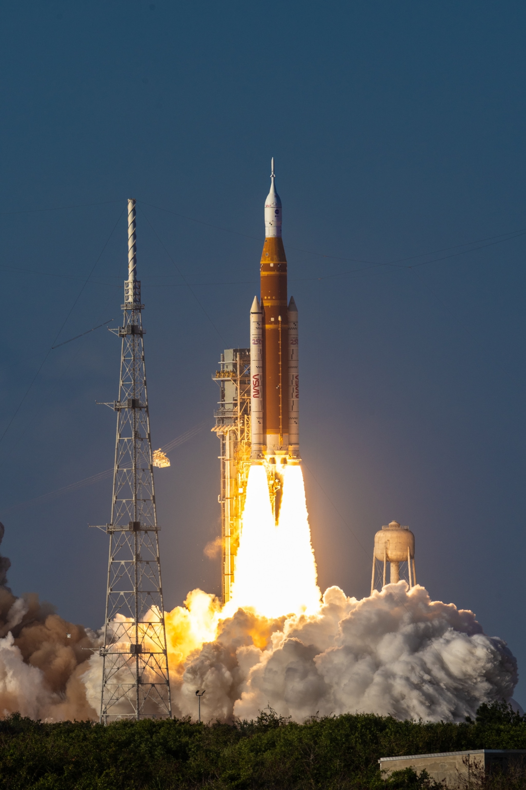 A powerful rocket launches into a clear blue sky, with bright flames and smoke billowing