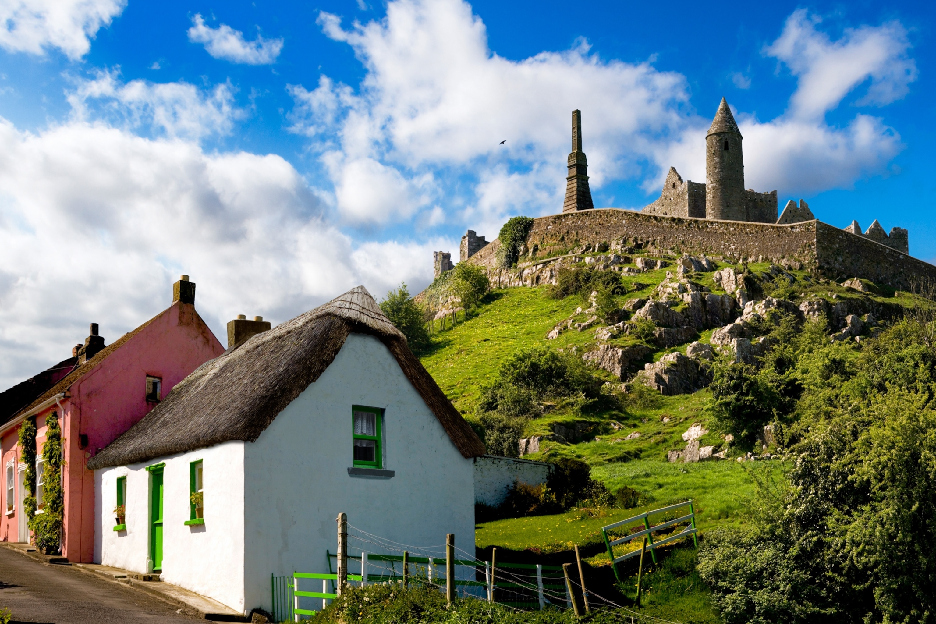 Small village houses along a quiet street, with the stone ruins standing atop a hill overlooking to village