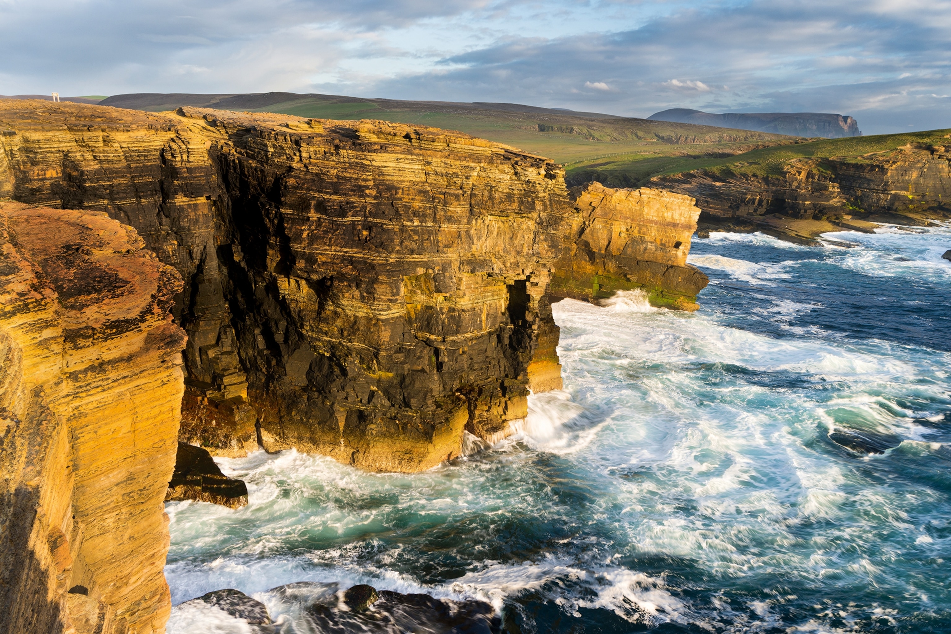 An aerial shot of a windy cliff with towering sea stacks and strong sunlight.