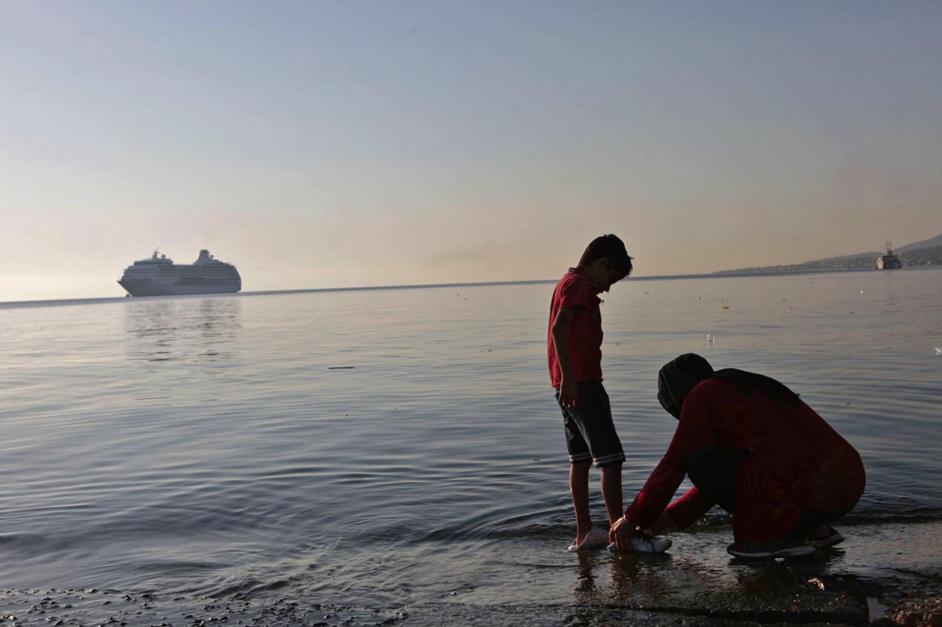 Afghan mother washes her son’s shoes in sea water in Mitilini, Lesvos, Greece