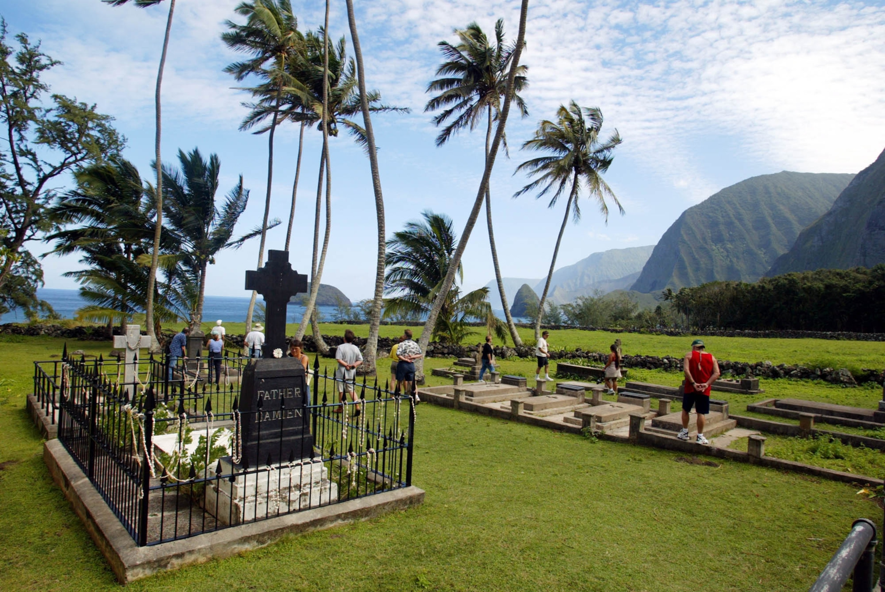 Tourists walk through a cemetery past the grave, left, of Father Damien at Kalawao, Hawaii