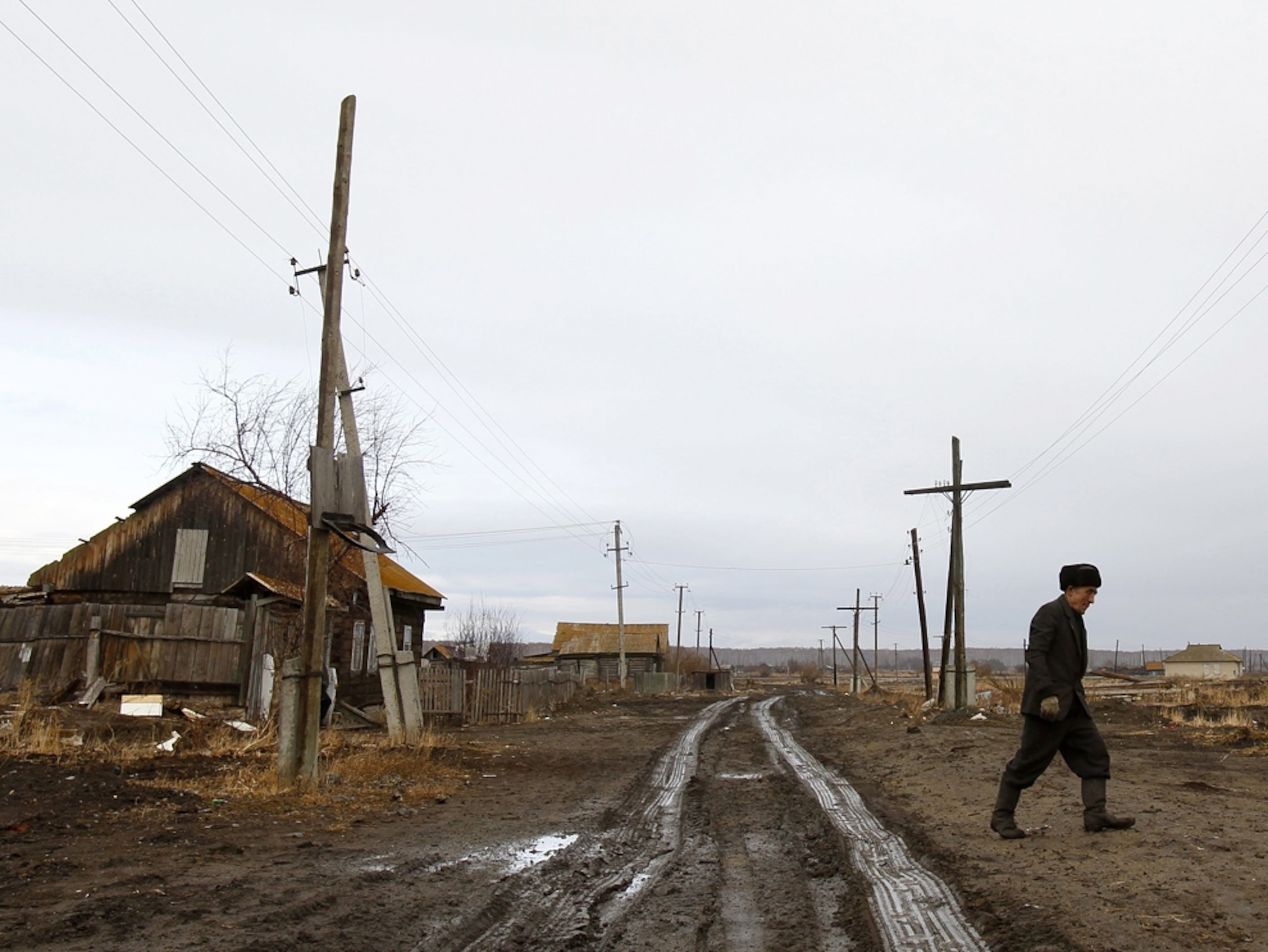 A man walks the muddy, deserted road that runs by his abandoned house.