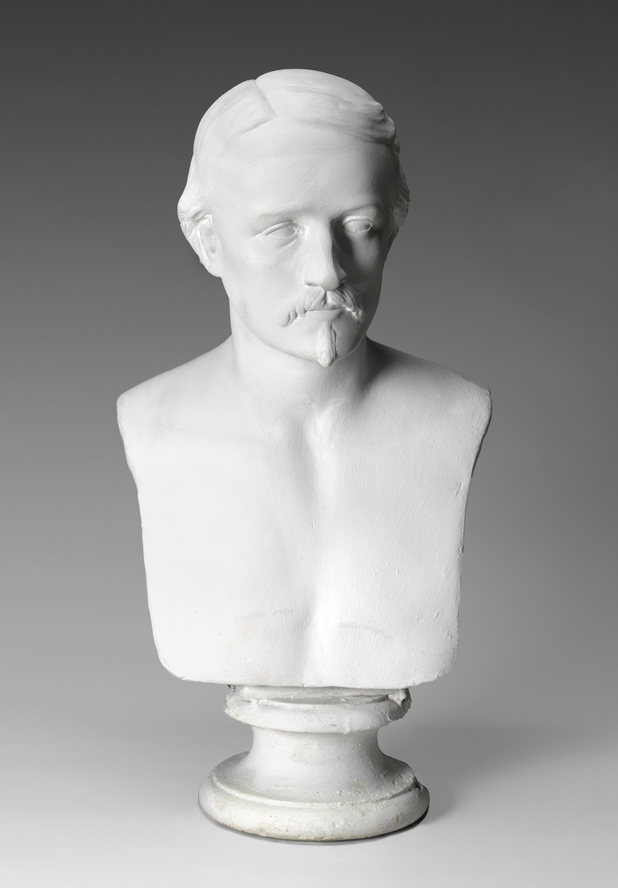 White marble bust of a man with a goatee and mustache against a dark gray background