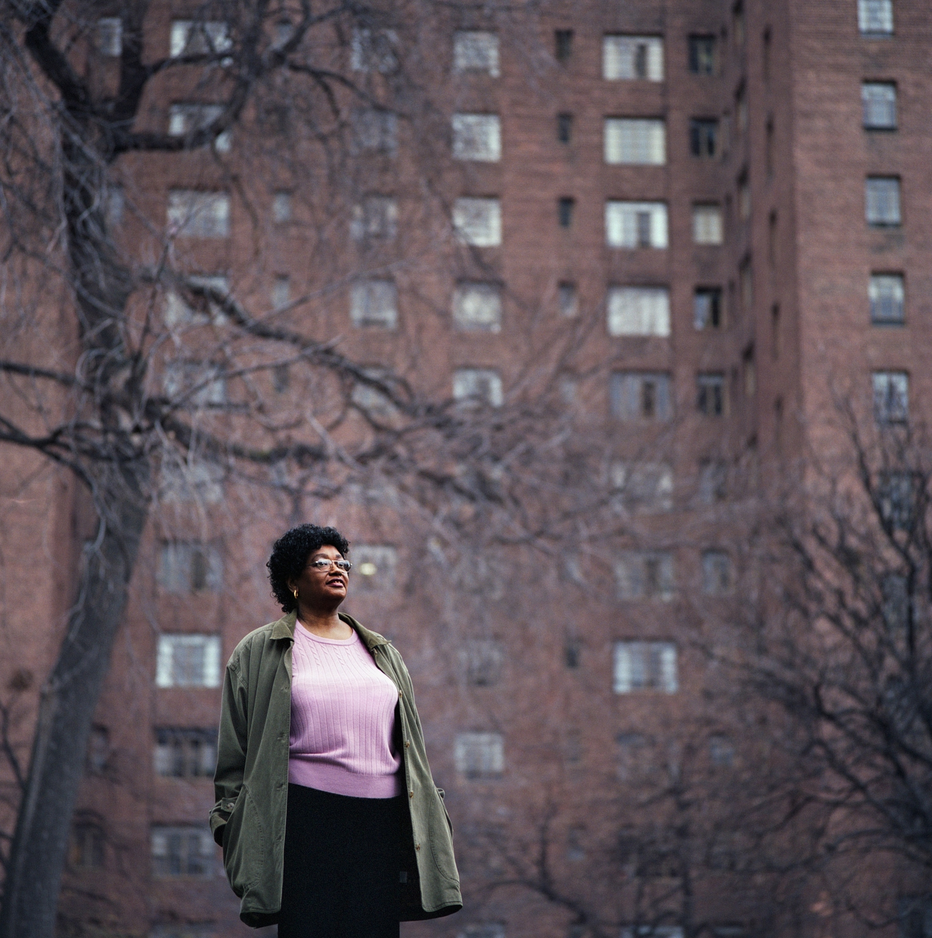 An African-American woman standing confidently in front of tall, brick apartment buildings with bare trees