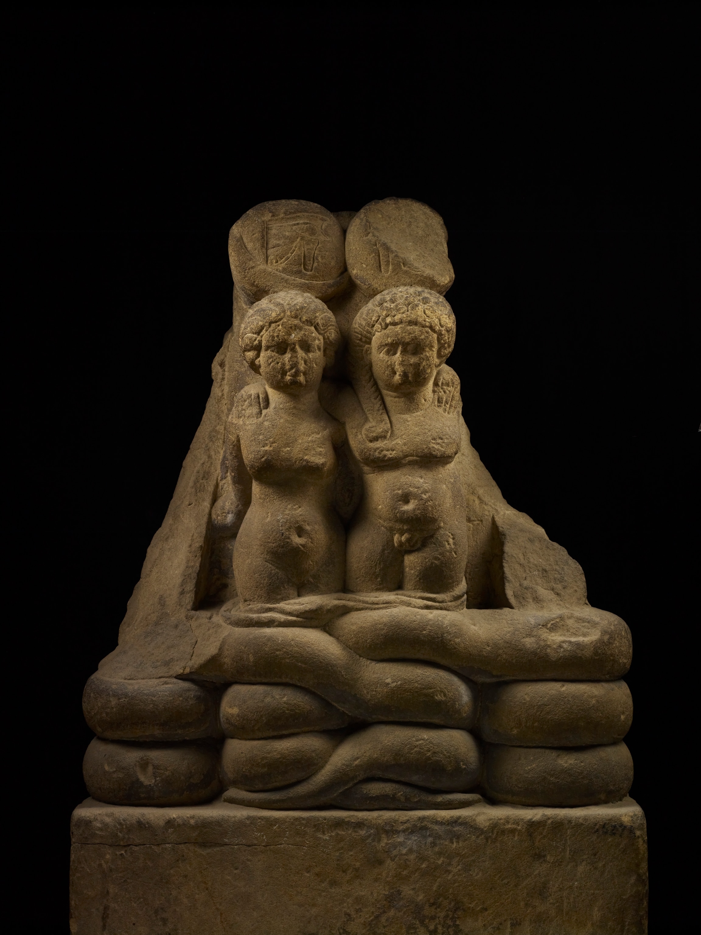 A stone statue of two figures against a black background.