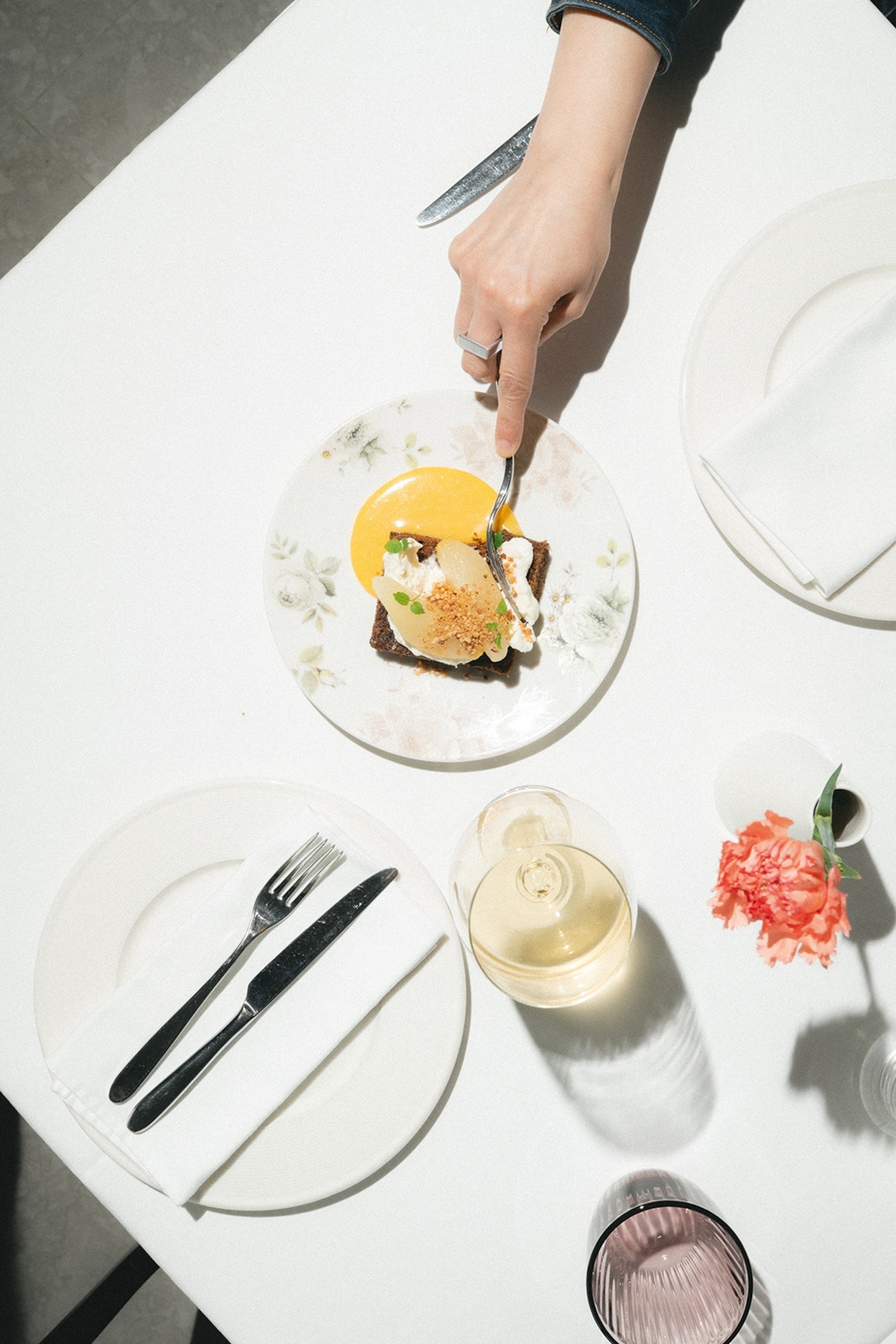 A dynamic food shot of a set table with linen and a plate of carrot cake with a hand cutting off a corner with a fork.