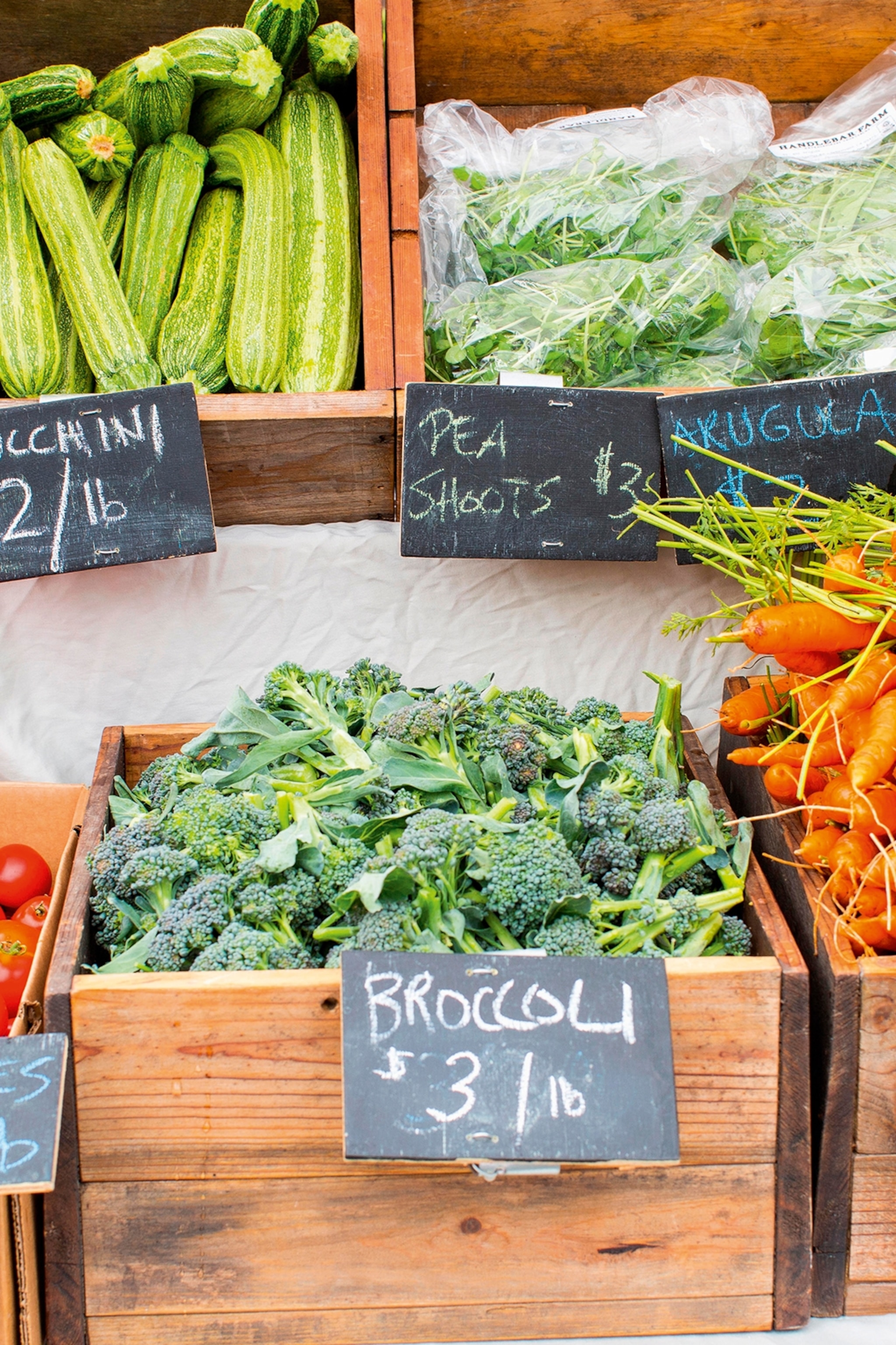 A close-up of fresh produce, including courgettes, carrots and tomatoes, in wooden crates at a farmer's market.