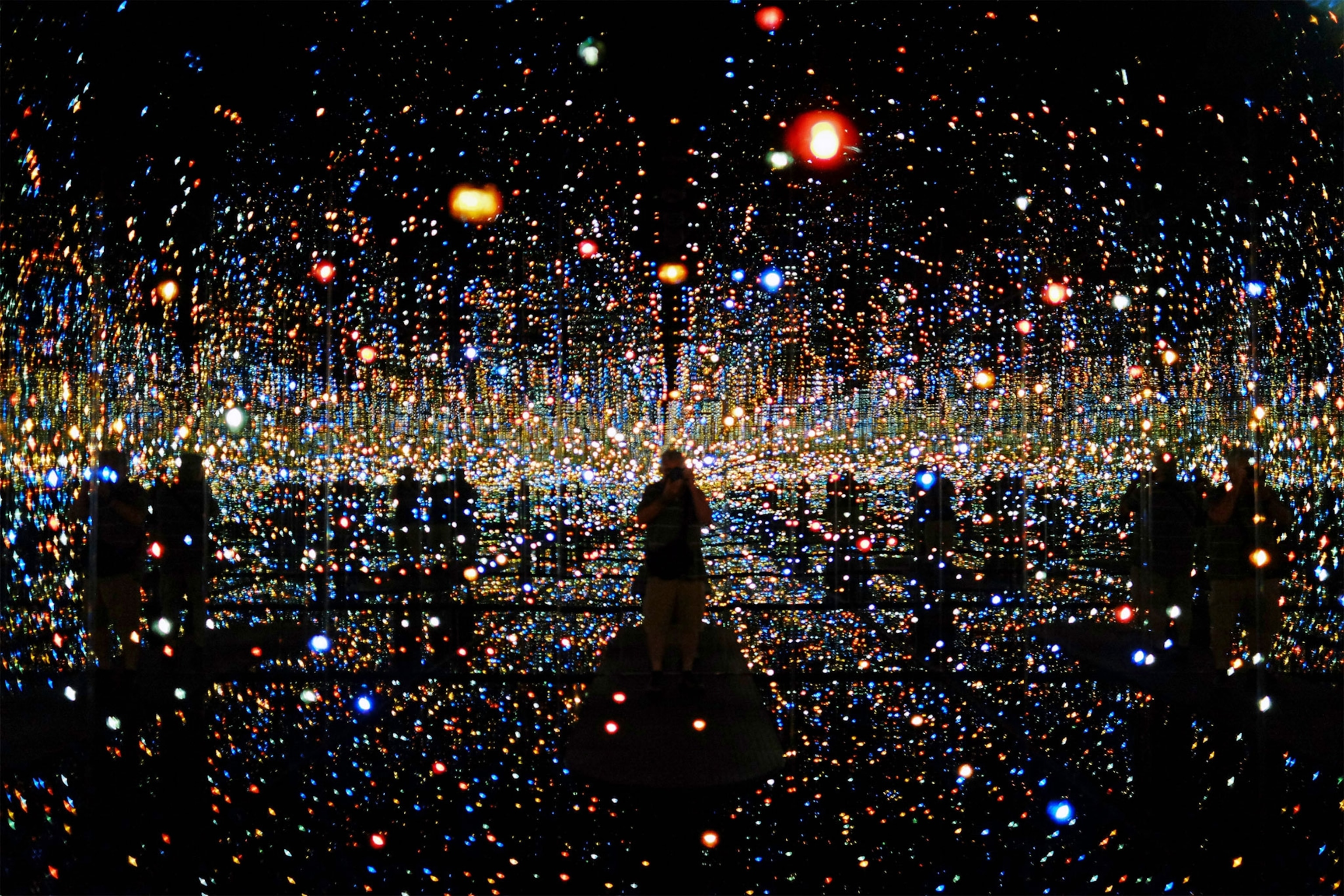 a person standing in an installation created by Yayoi Kusama