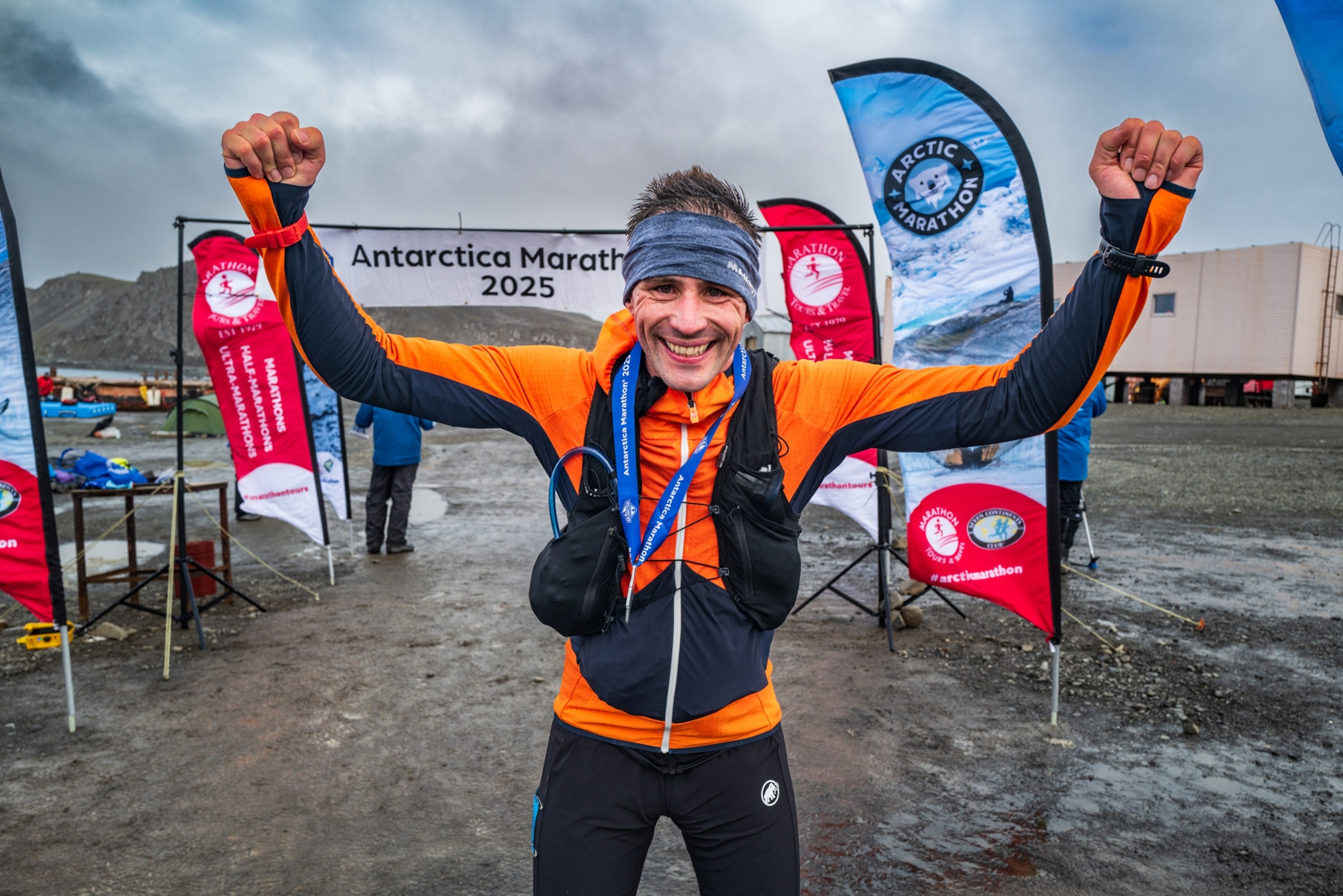 a man with arms raised and a smile on his face with a finish line banner above him in the background