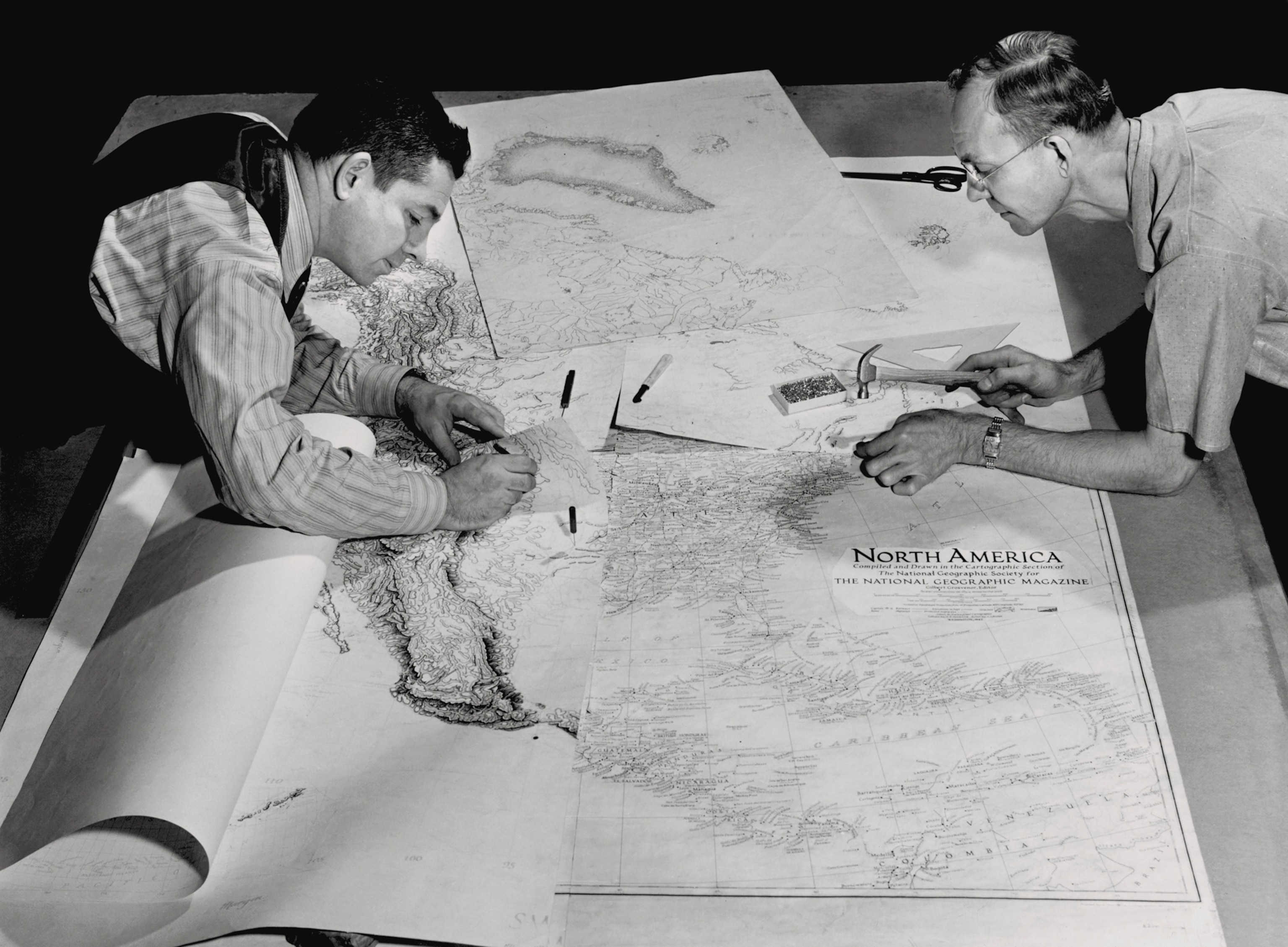 business Two people lean over maps and work on them.