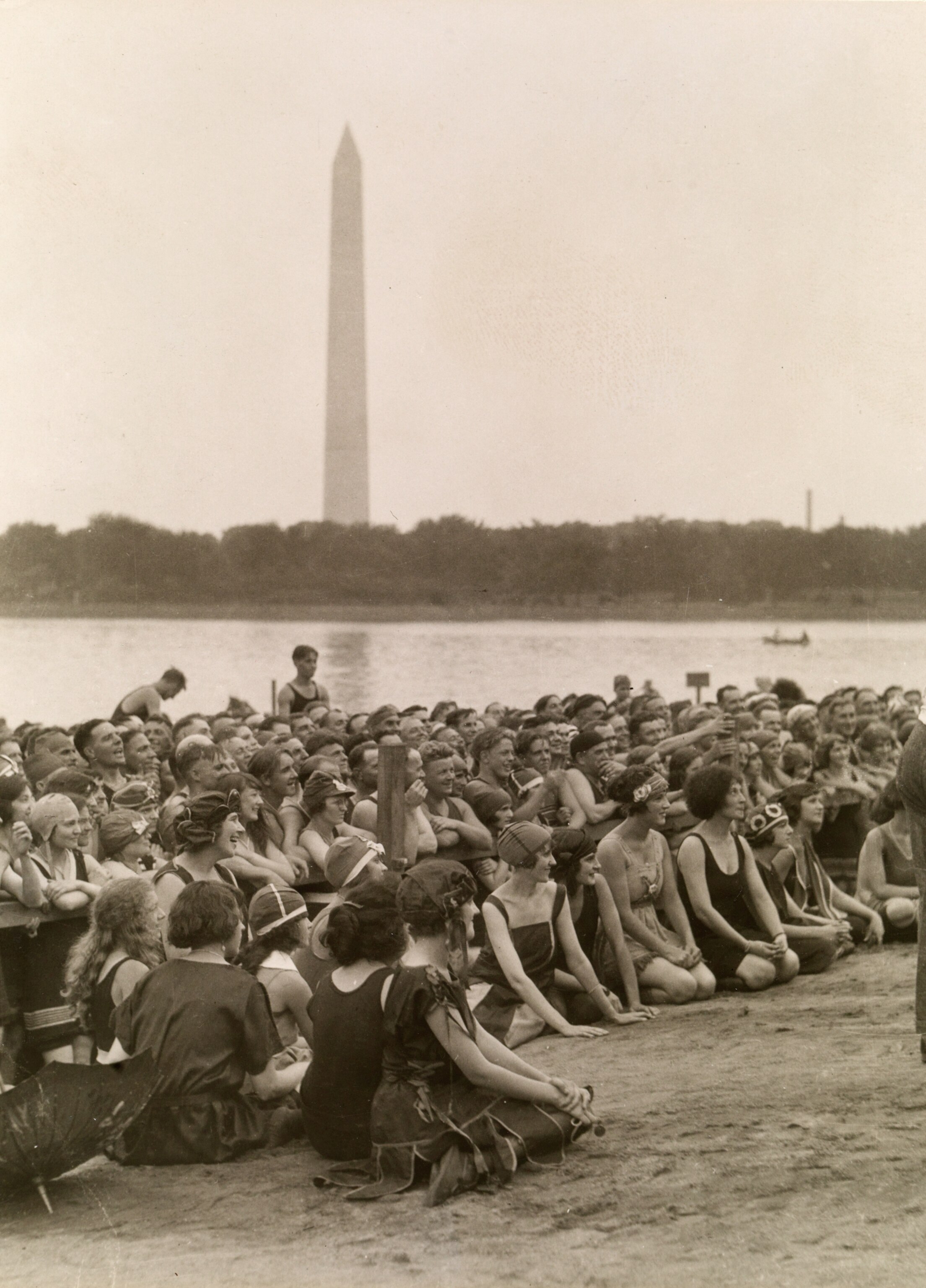 A large crowd of women sit on the sand; Washington Monument in the distance, 1922.