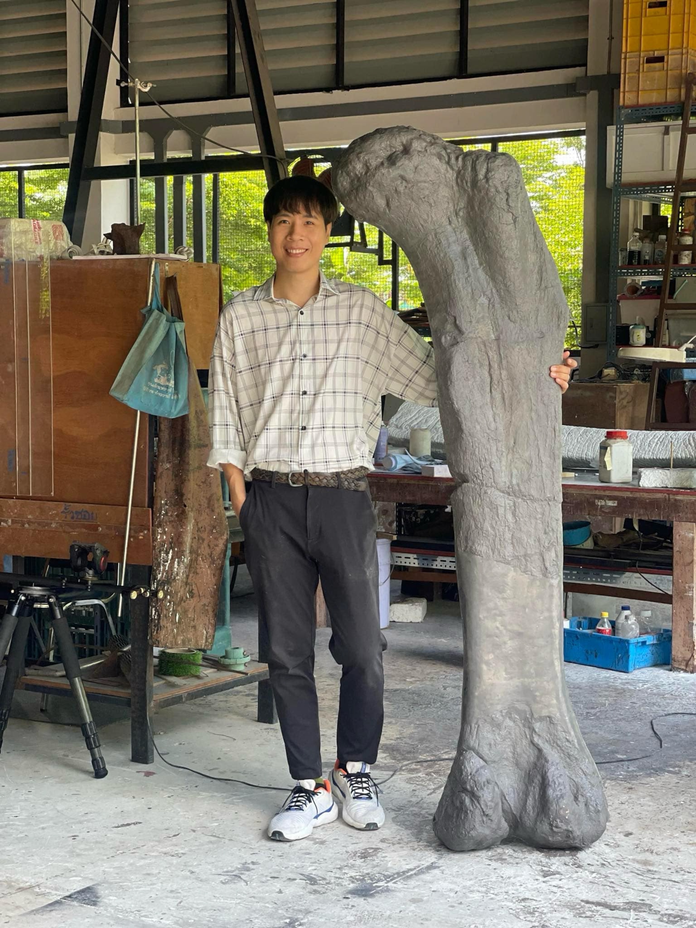 A person smiling and standing next to a large dinosaur bone in a workshop