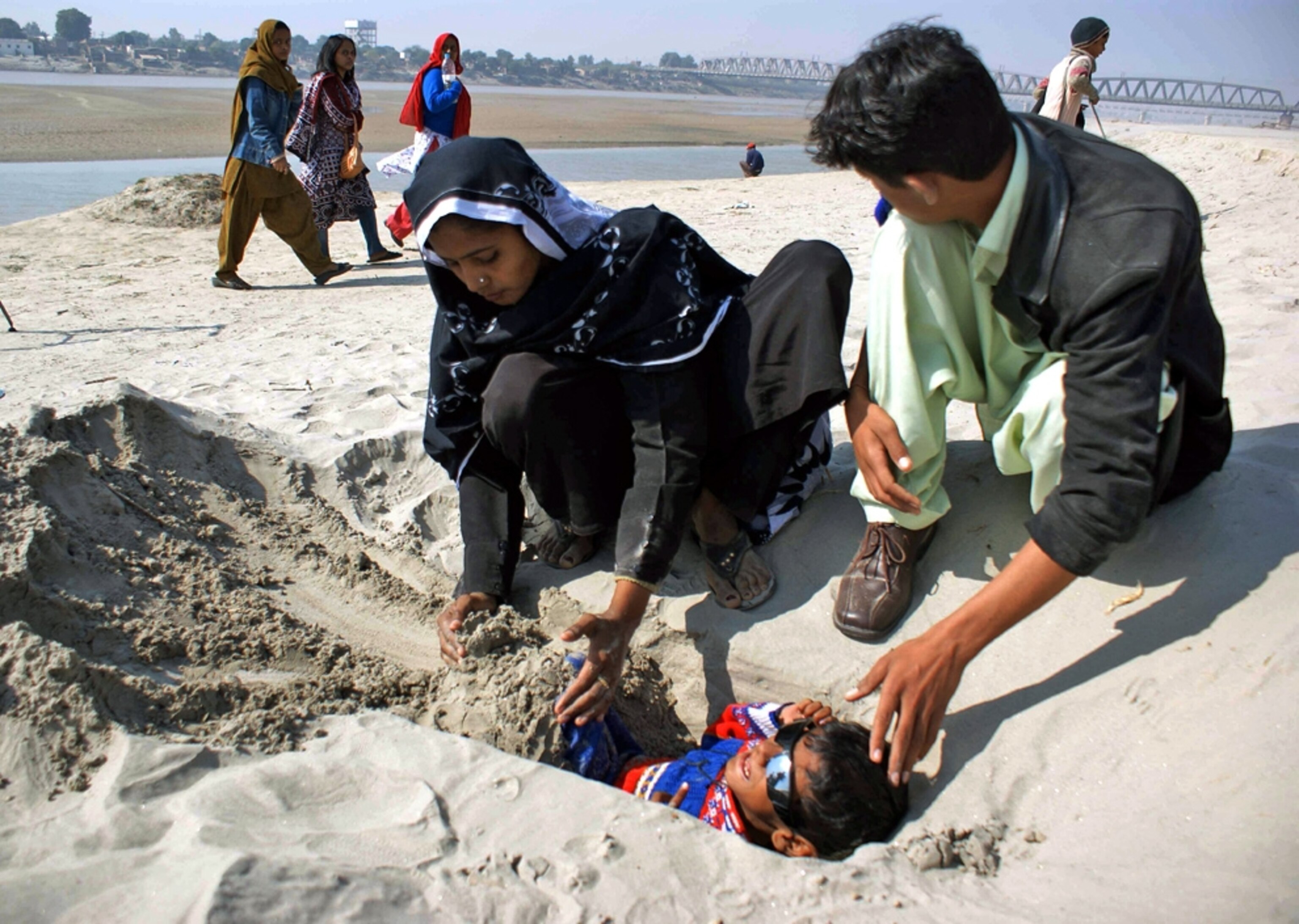 Boy being buried in the sand during a solar eclipse (picture).