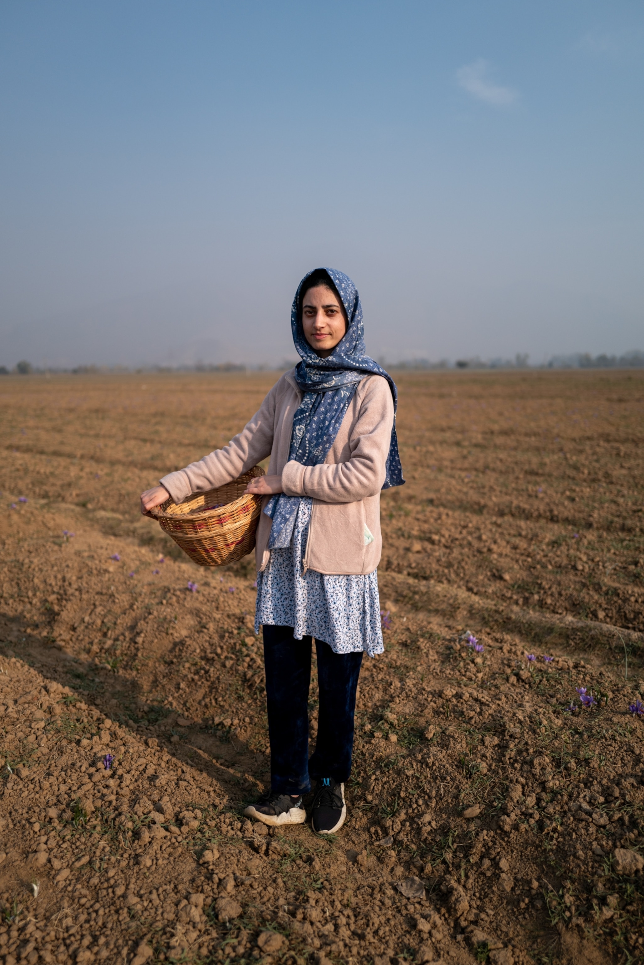 A woman holds a basket standing in a field.