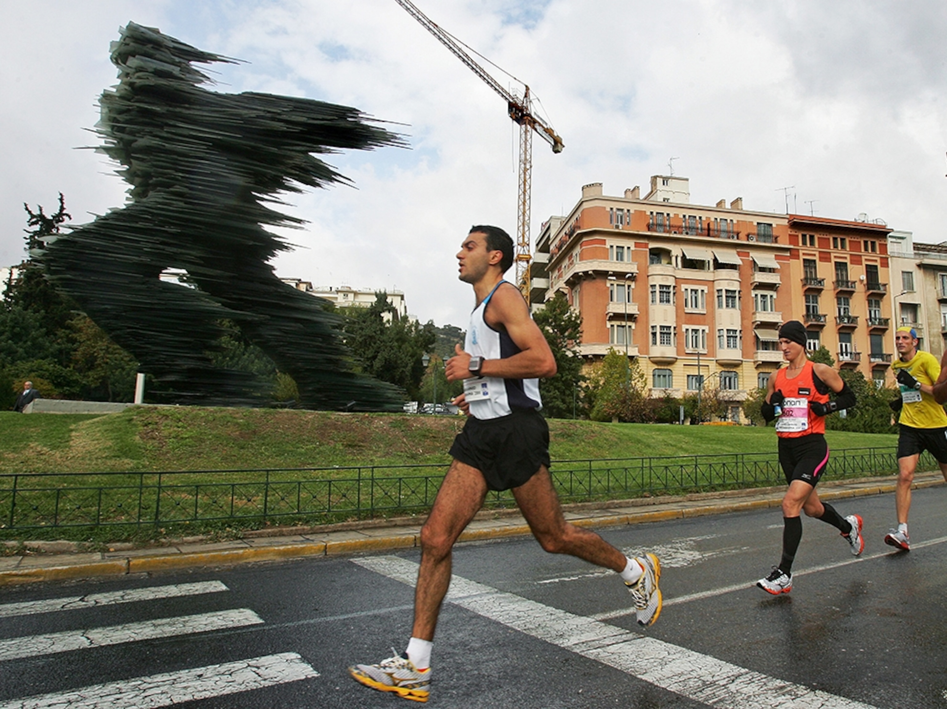 runners passing the runner sculpture in the Athens Classic Marathon