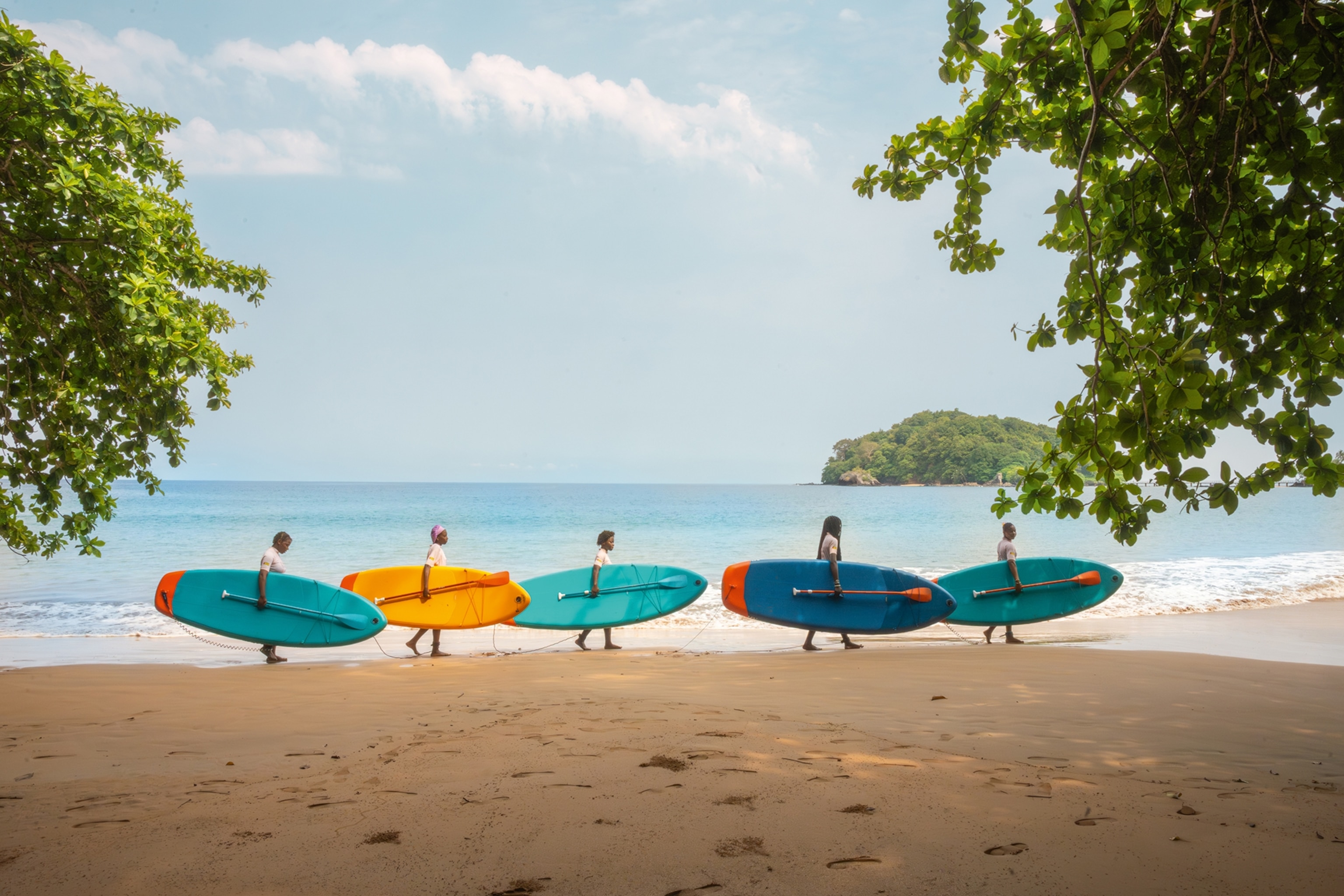 A landscape shot of a beach with a group of girls walking past in a line carrying surfboards.