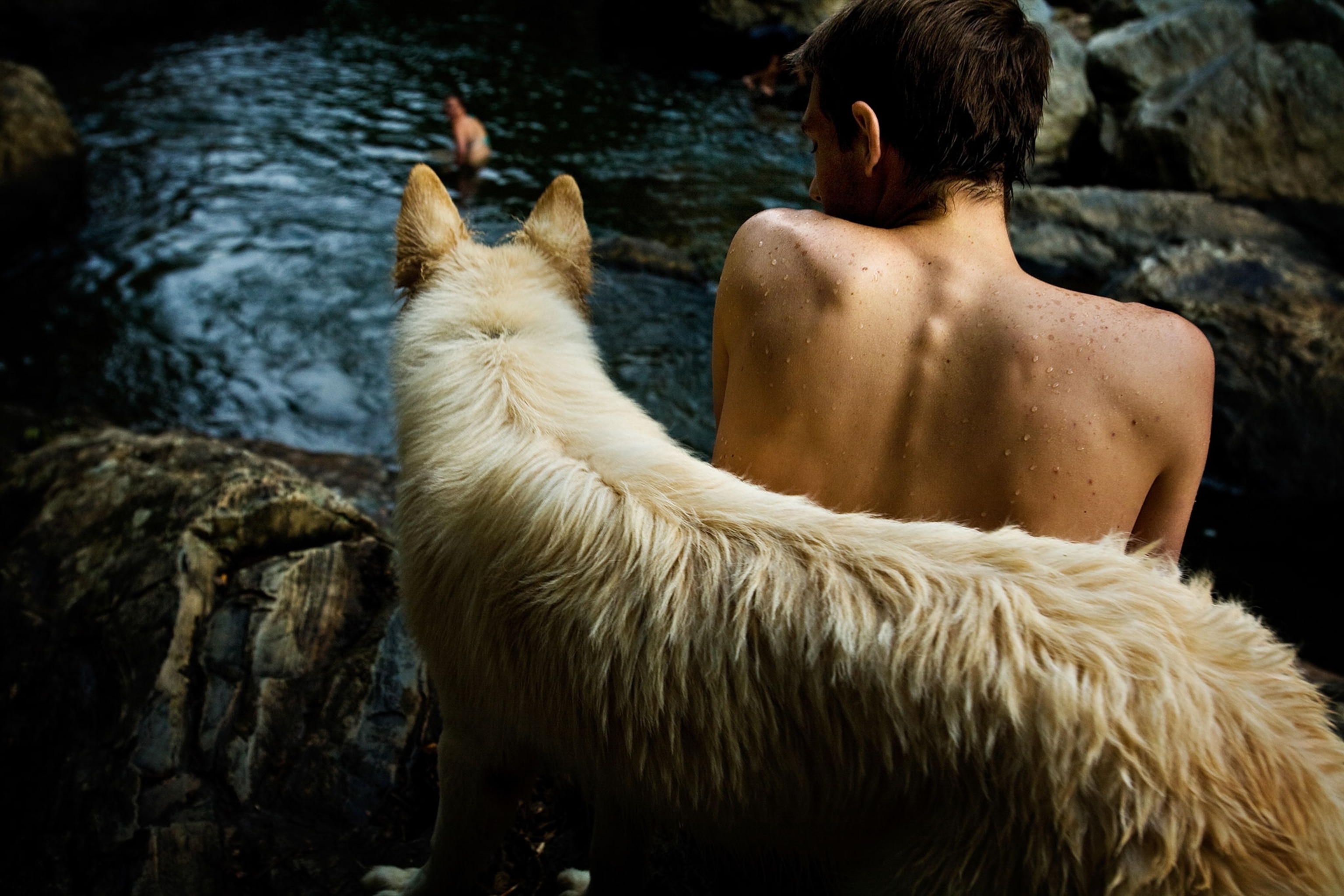 a dog and boy resting next to a swimming hole