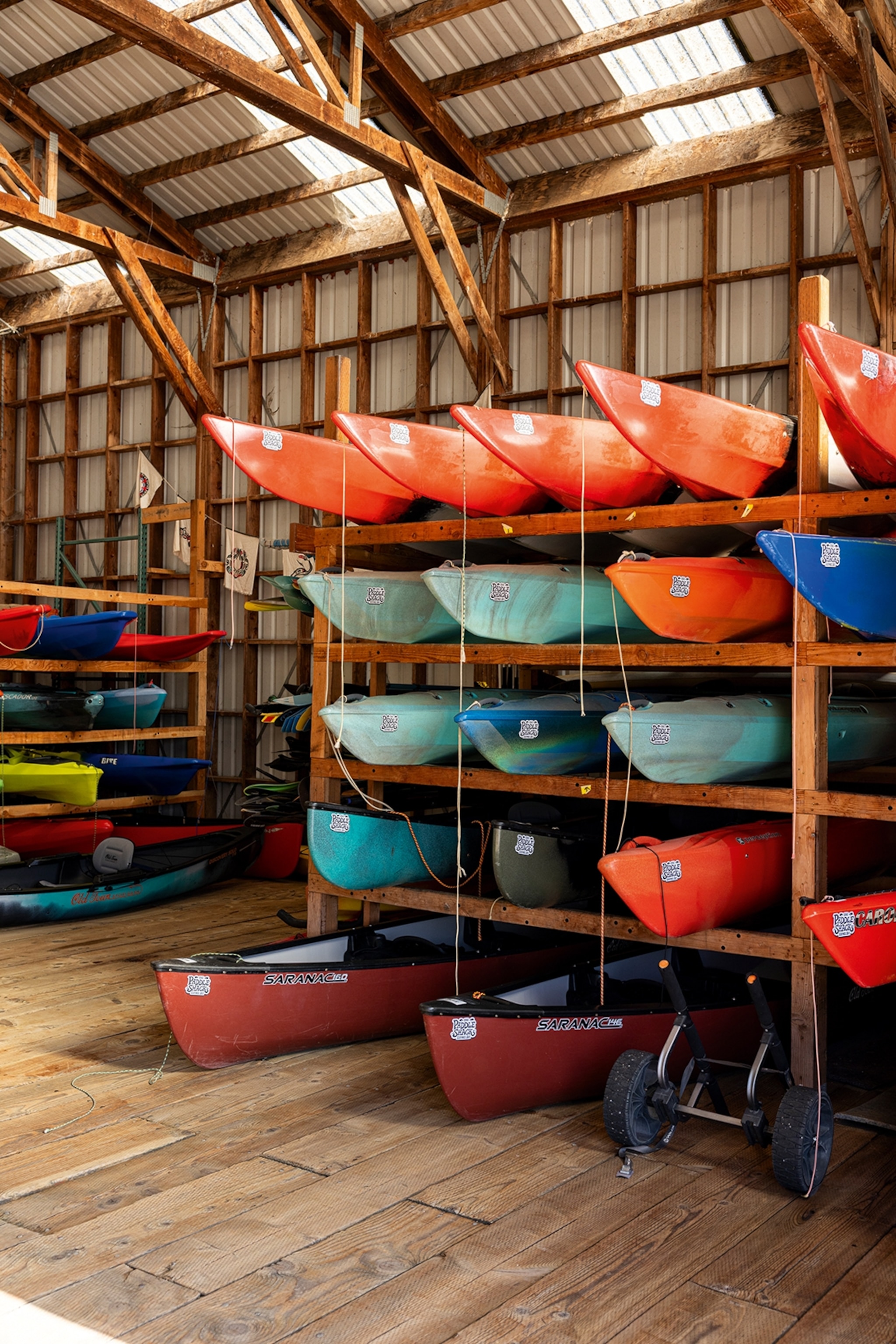 The interior of a wooden storage hut with kayaks stacked on wooden shelving systems.