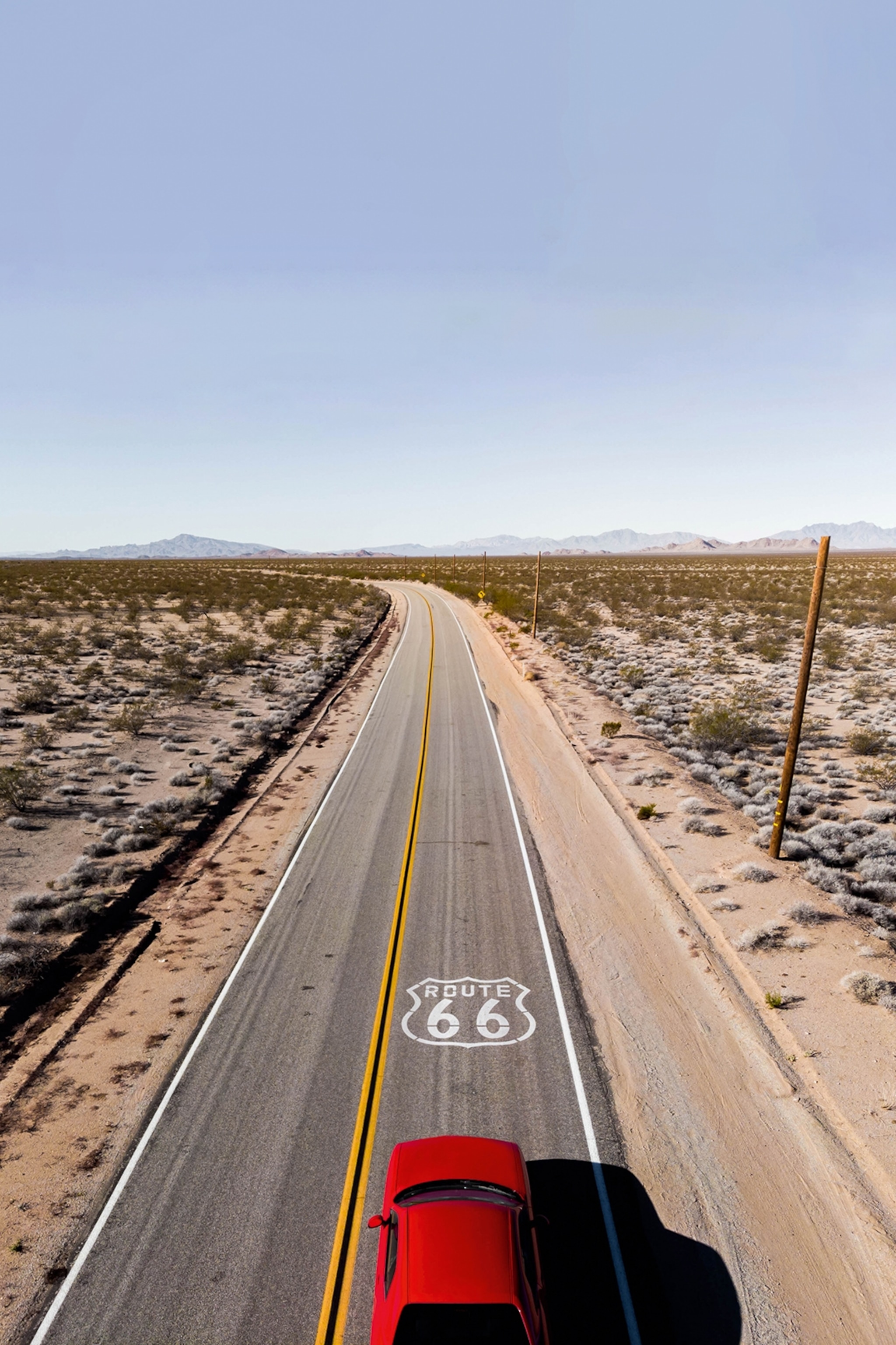 A long stretch of road leading through flat, bushy lands.