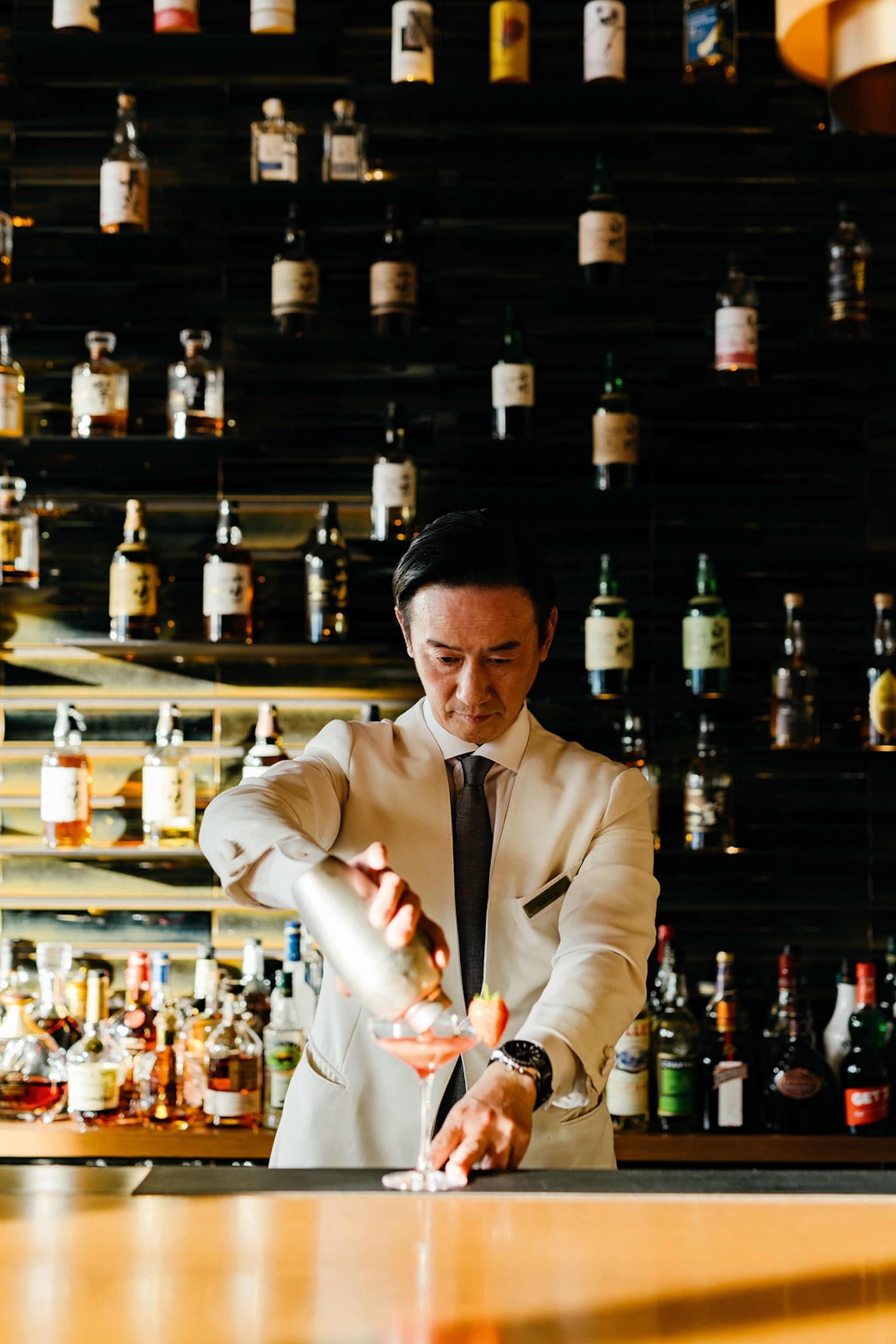A bartender pouring a drink with strawberries into a cocktail glass.