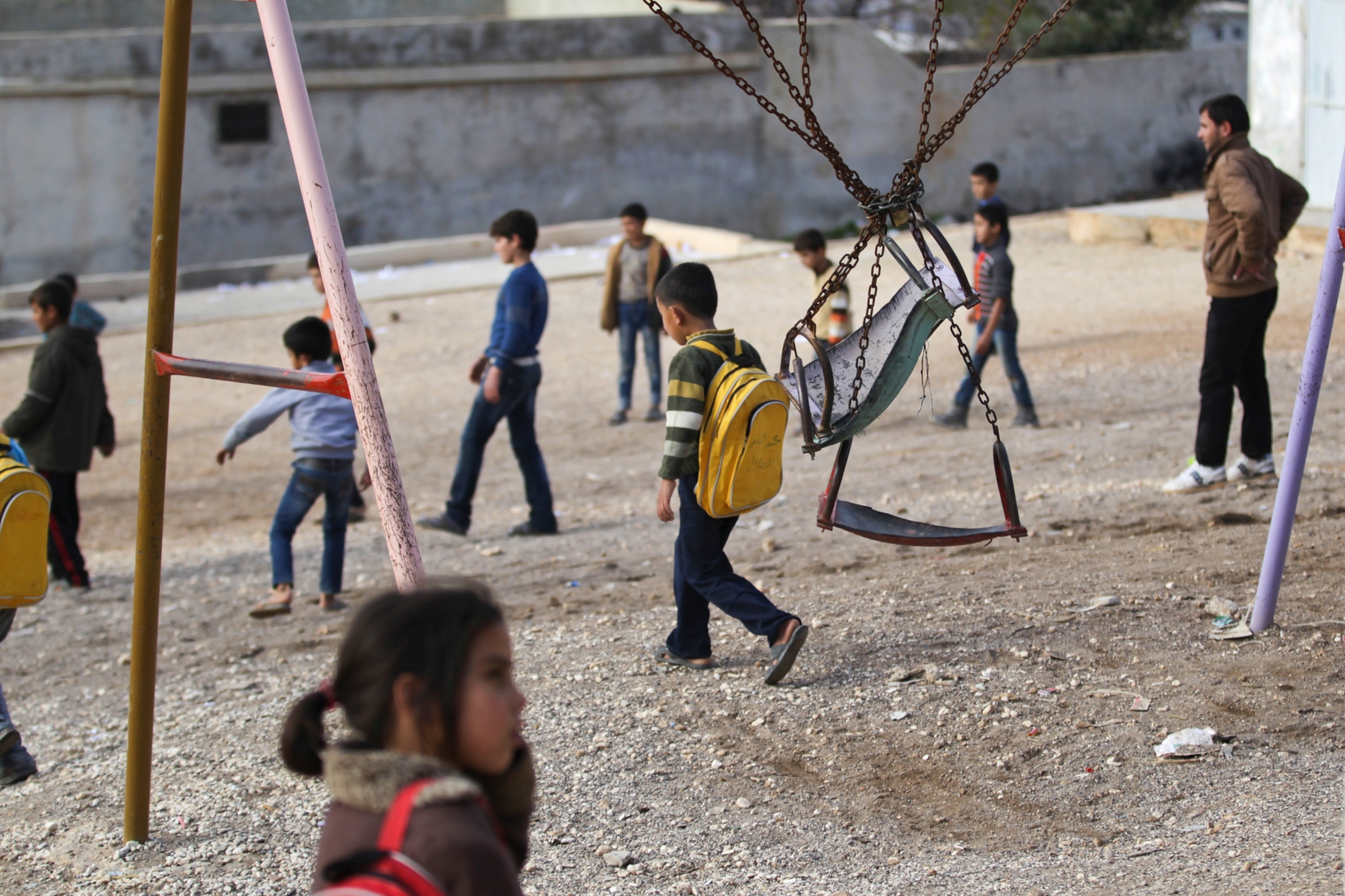 a refugee wrapping himself with a blanket as he stands on a muddy path during wintry weather.