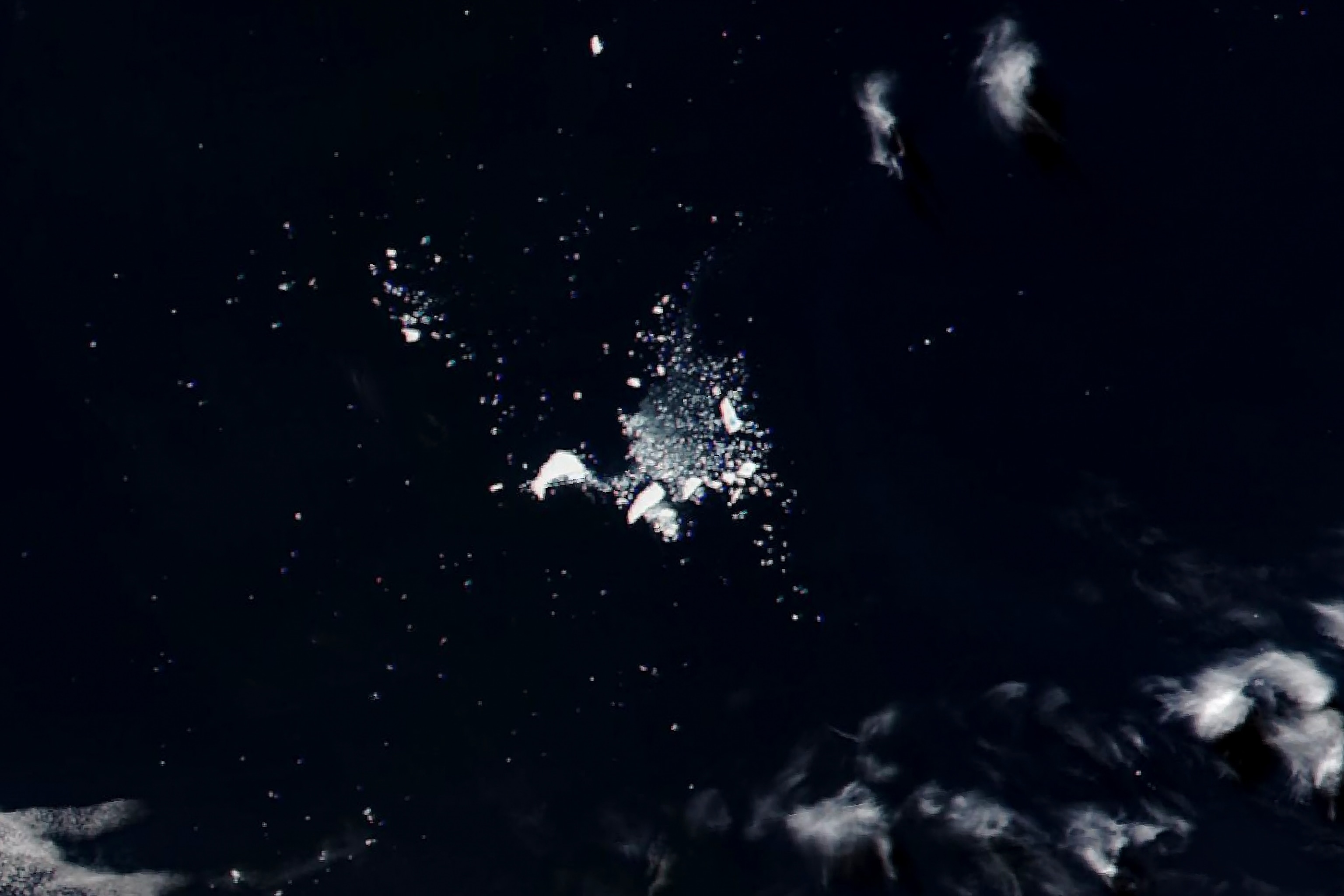 Satellite image of crumbling white icebergs scattered in a deep blue ocean.