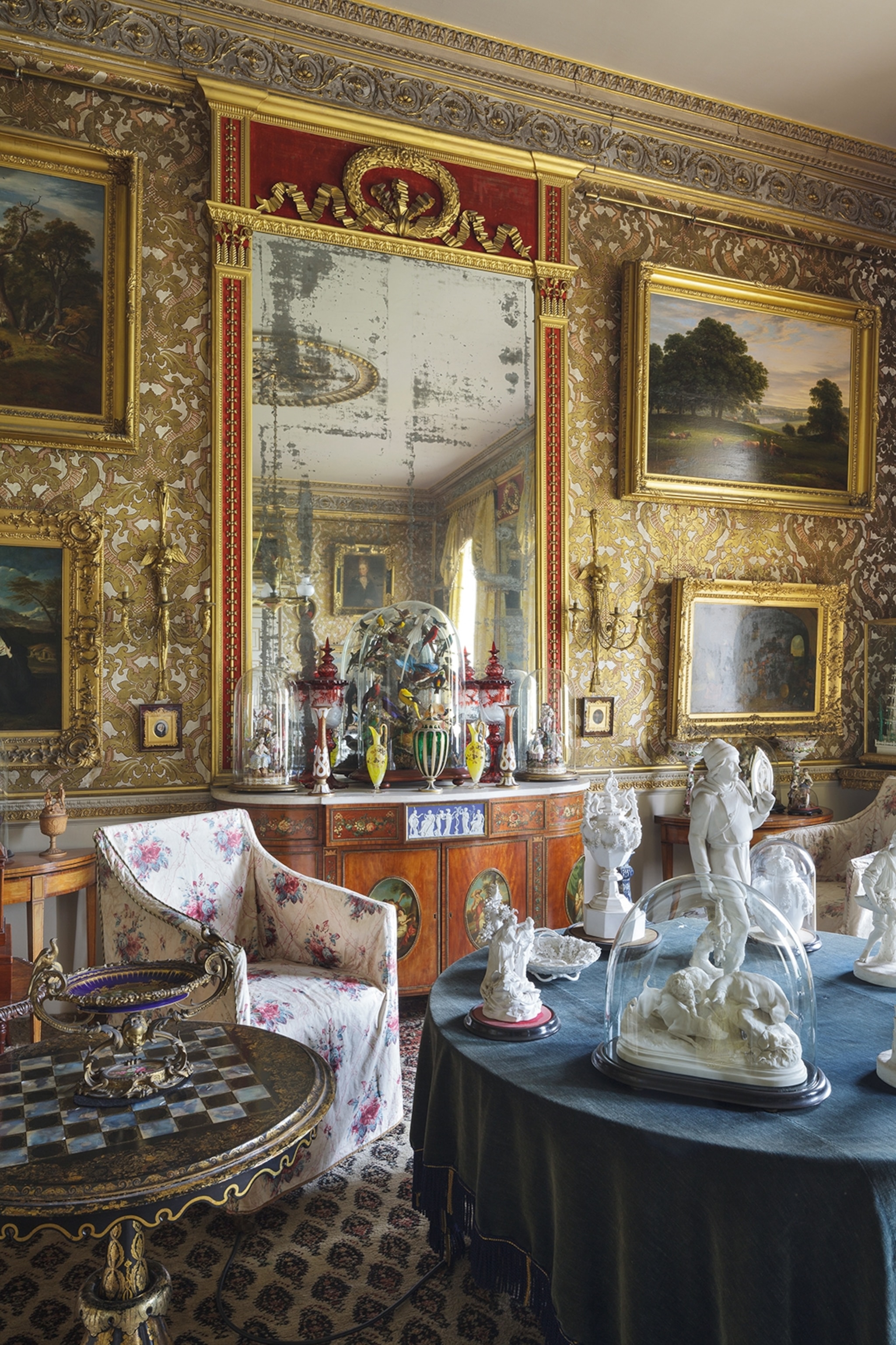 An opulent sitting room with sofas, armchairs and gold-framed art hung on the walls.