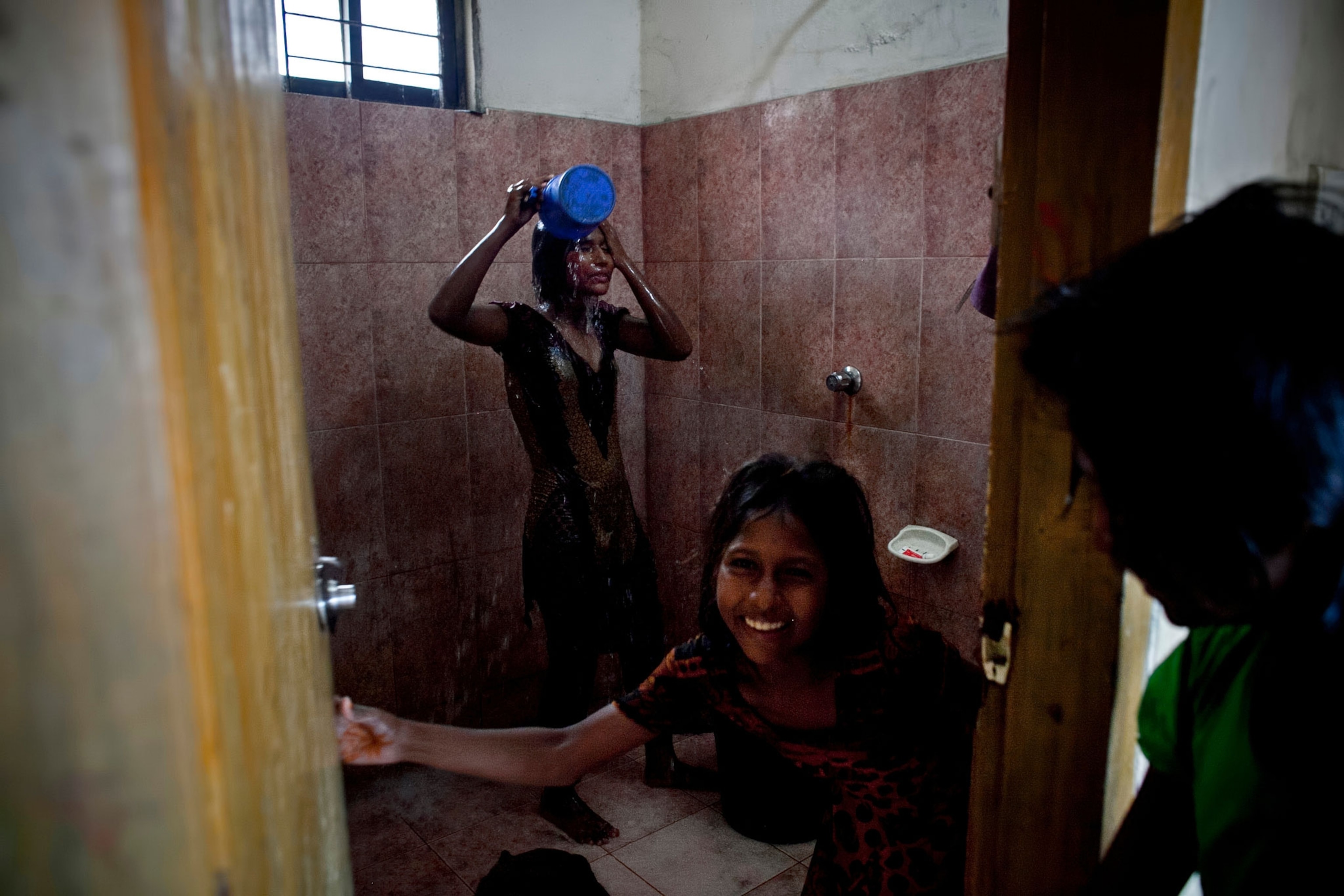 Aisha laughs as Sumi, 11, rinses off in the shower after surfing.