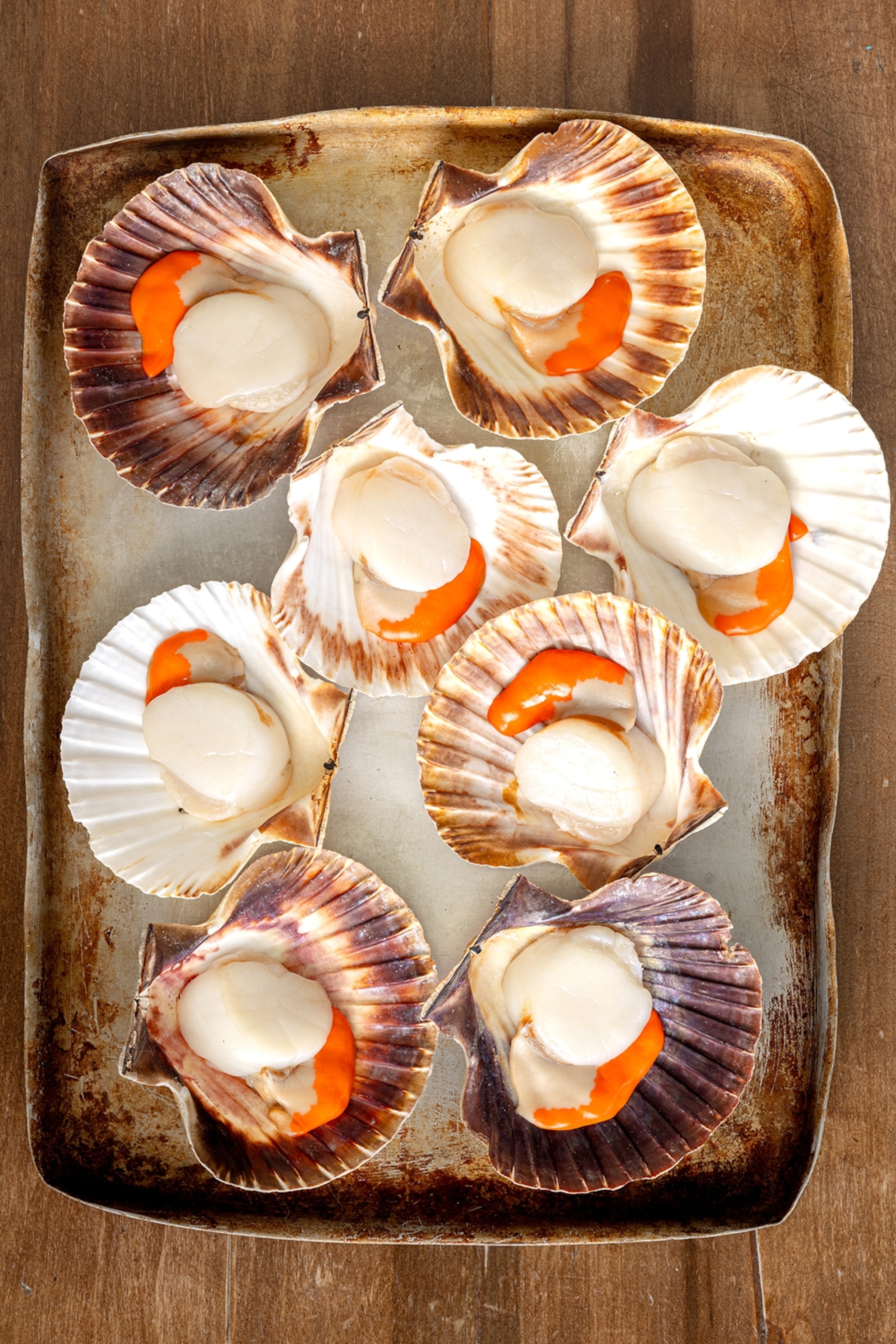 A baking tray of cooked scallops in their shells.