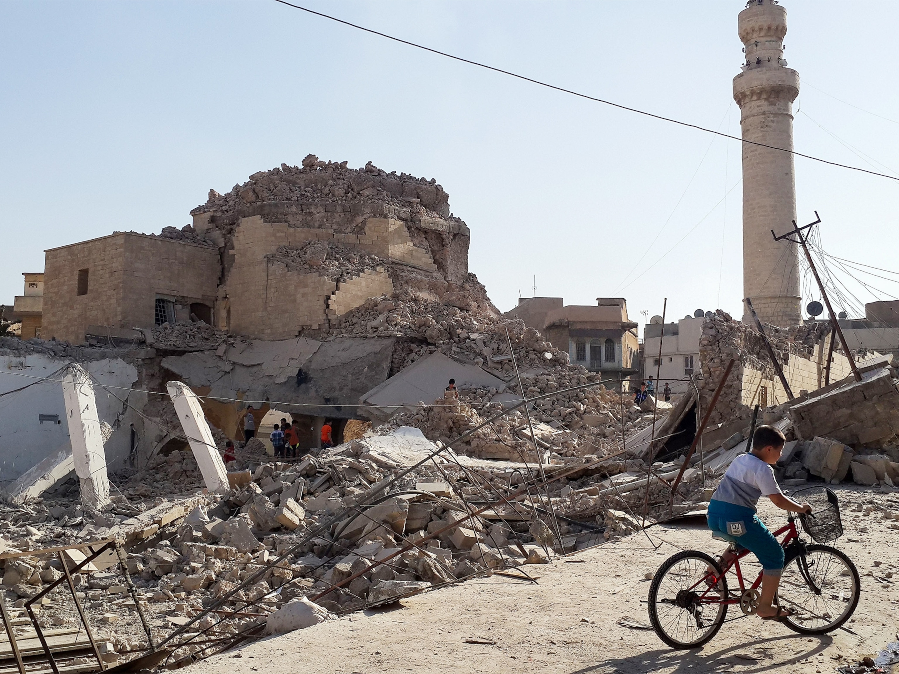 a person riding a bicycle in front of the destroyed Prophet Jirjis mosque in central Mosul.