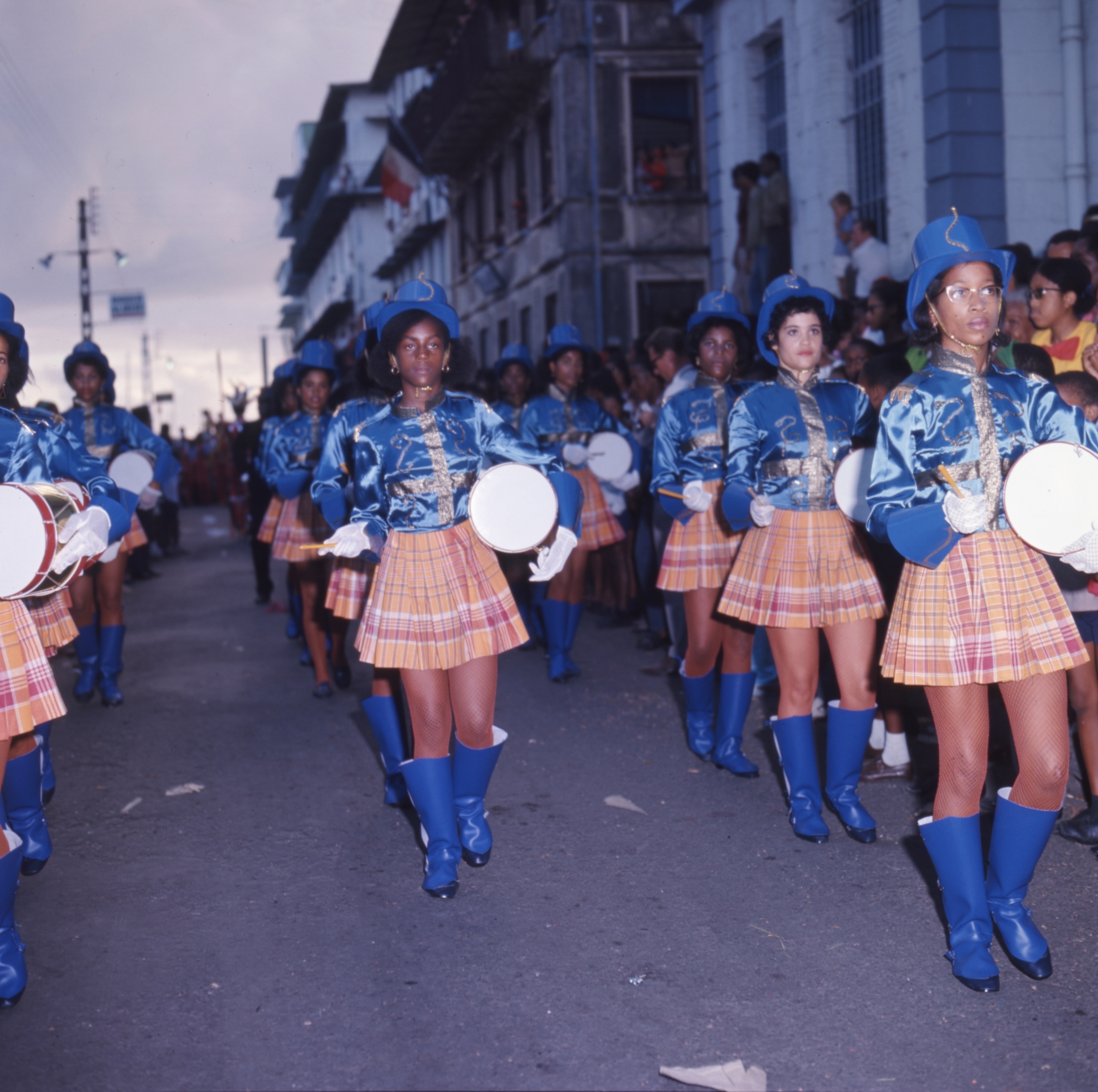 A group of girls in blue shirts hats and skirts with drums