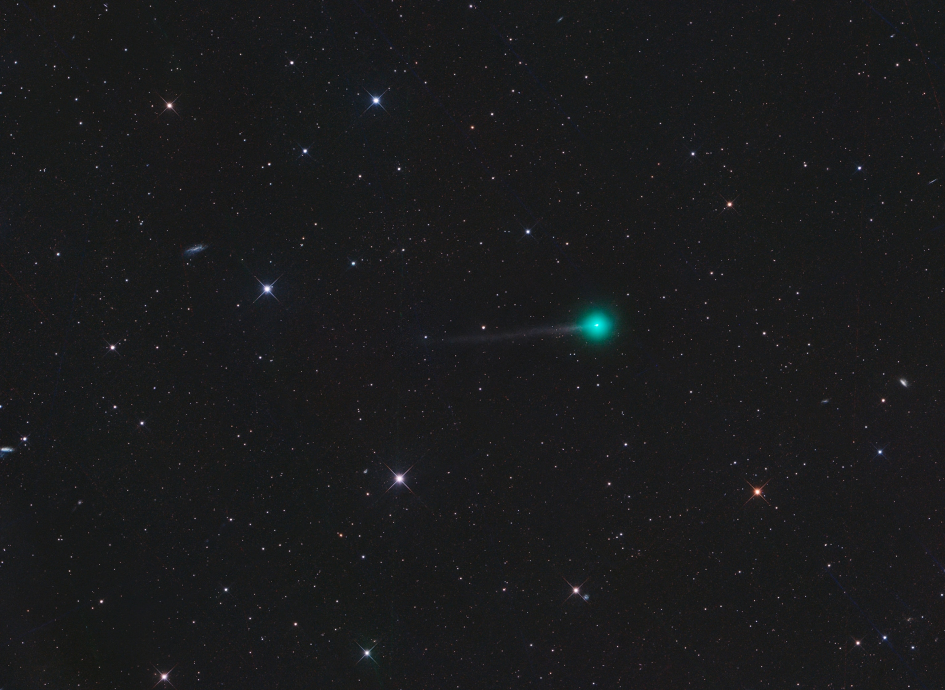 Bright green comet with a faint tail surrounded by numerous stars against a dark night sky.