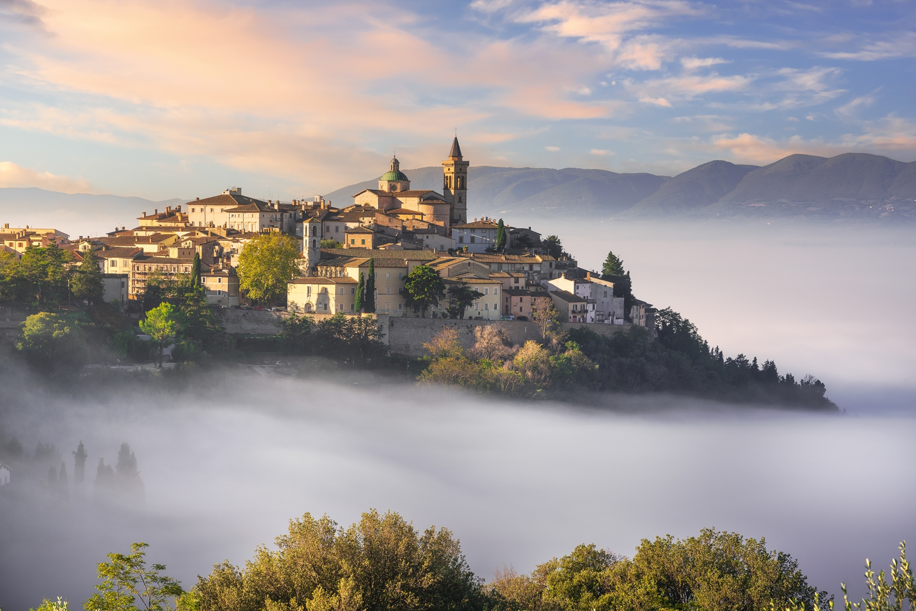A castle and stone town atop a hill in the morning light with mist hanging in the valley below.