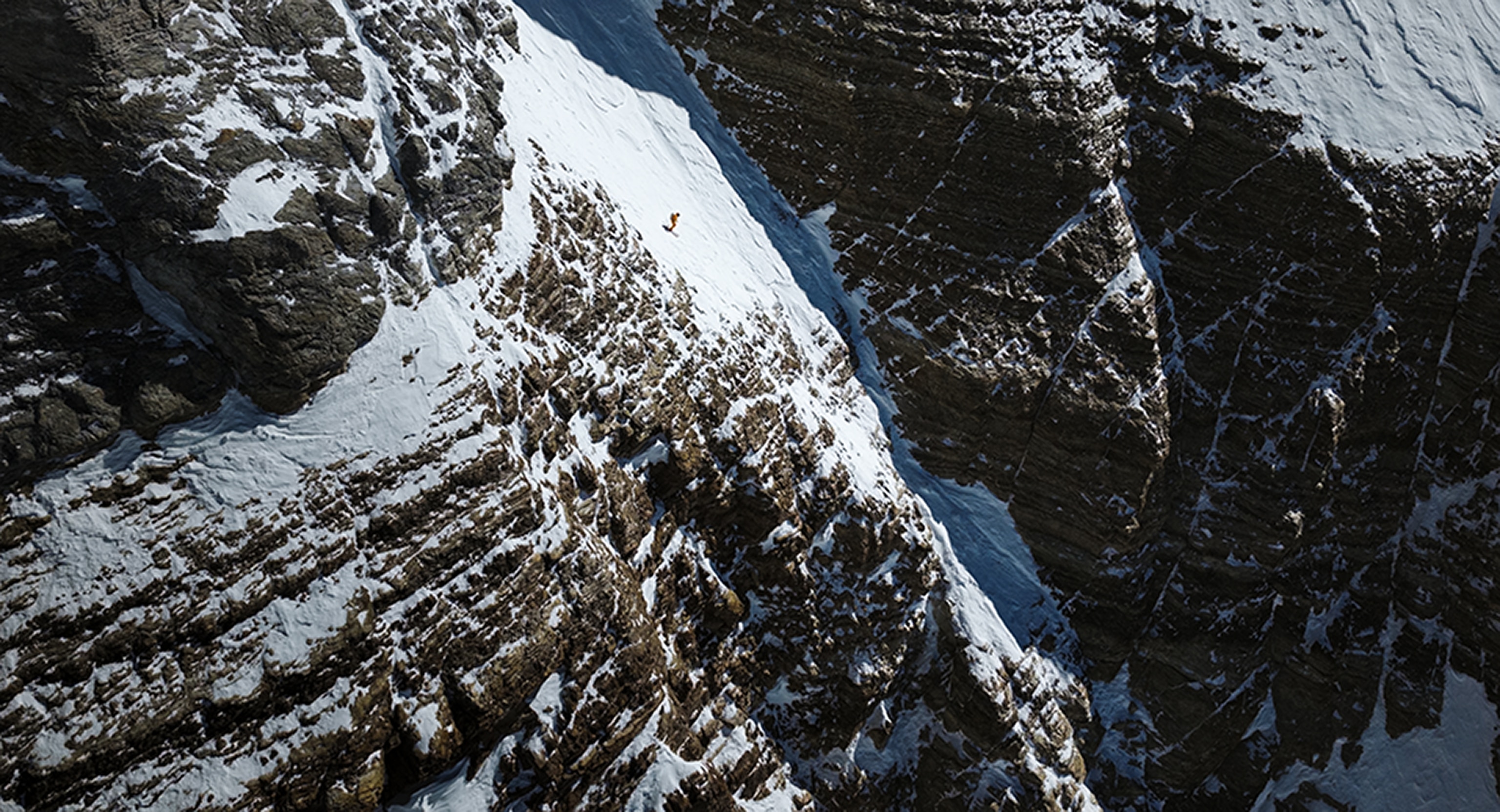A man skis down a narrow patch of snow on an extremely steep slope between huge areas of ragged rock.