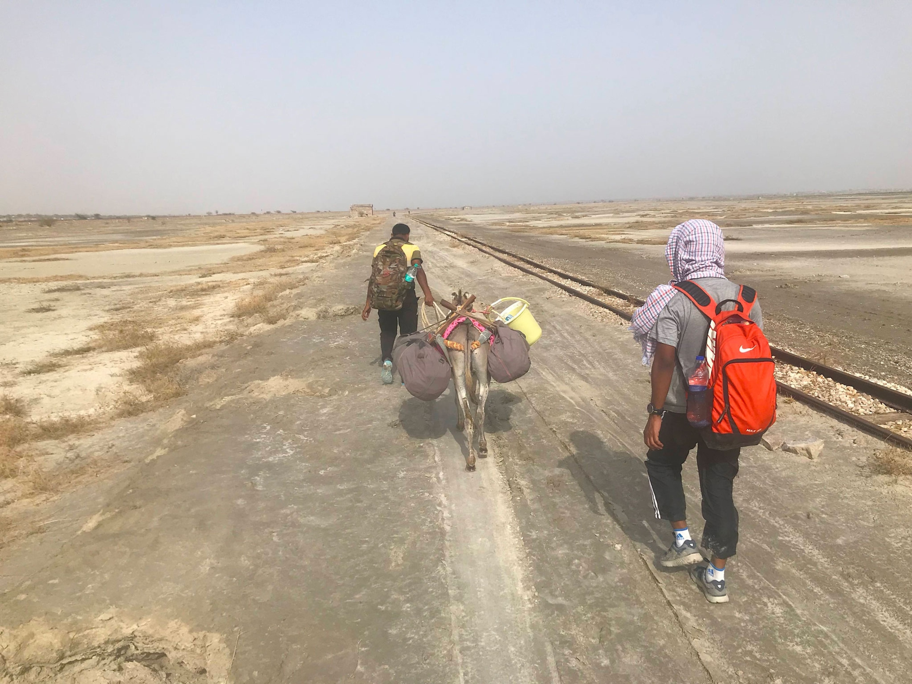 two men and a donkey walking down a dry dirt road.