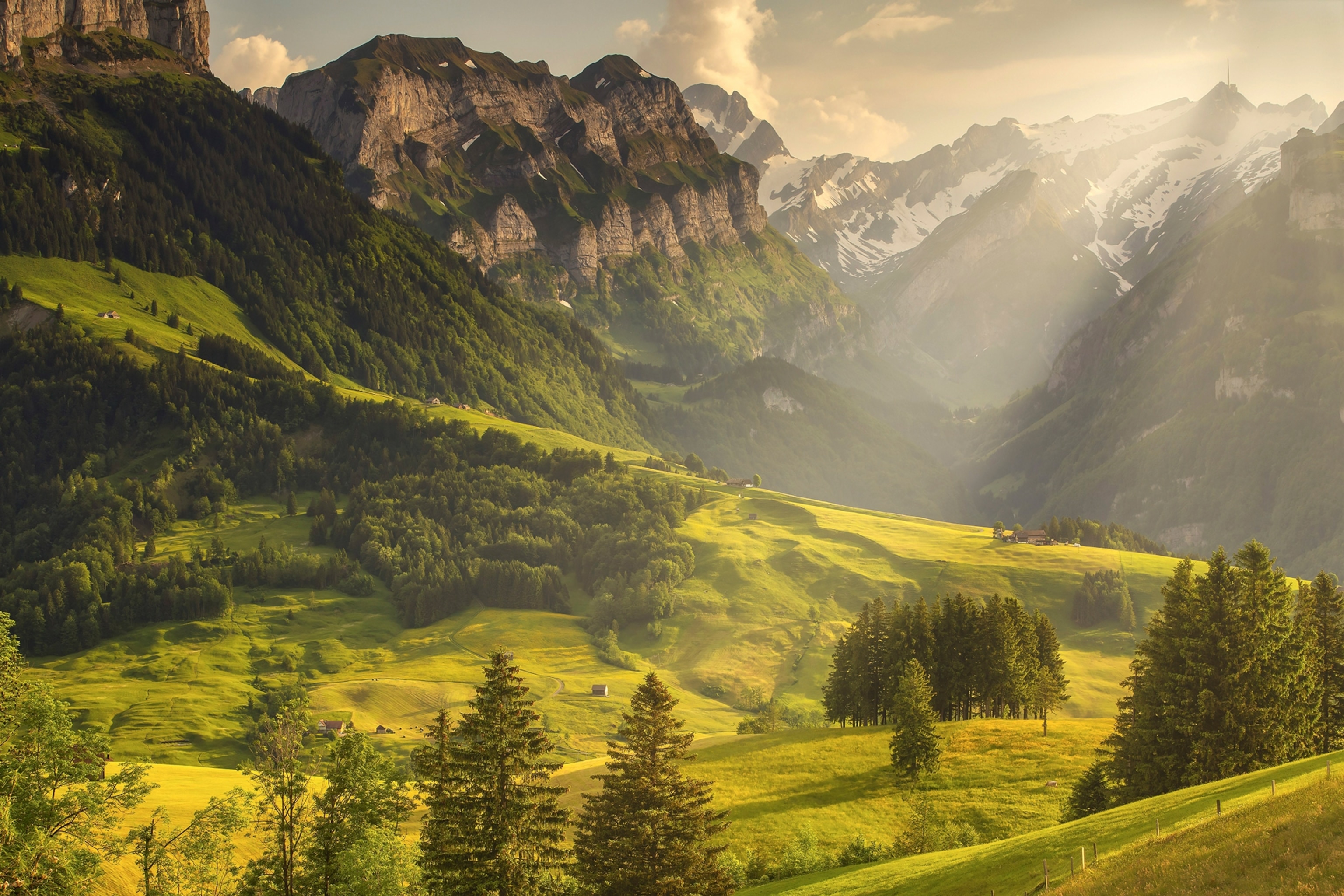 A scenic mountain valley with sunlight peaking dramatically through clouds in the sky.