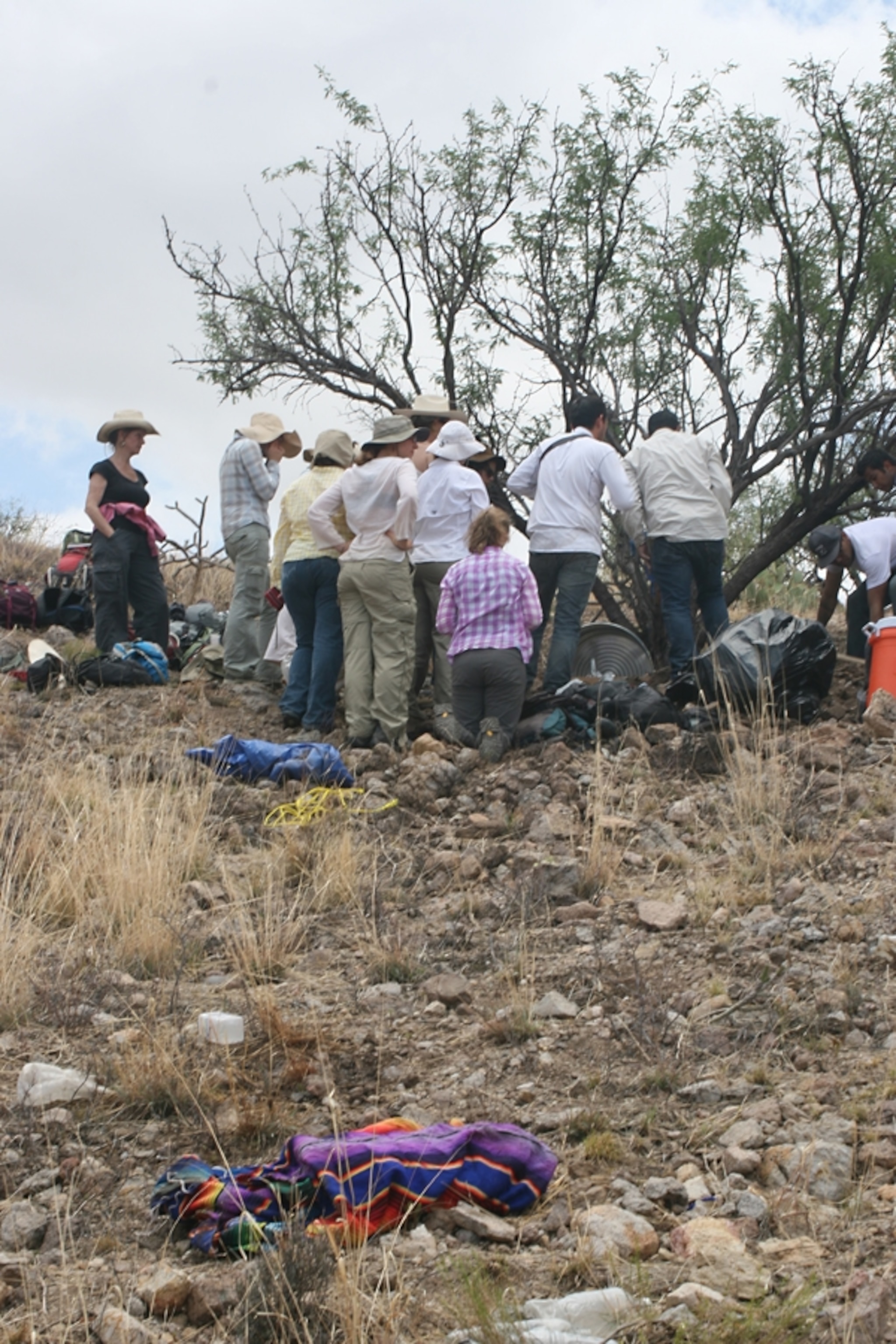 Some researchers pray before a shrine to a dead migrant. In the foreground, the blanket that covered her body. Photo by Jason De León.