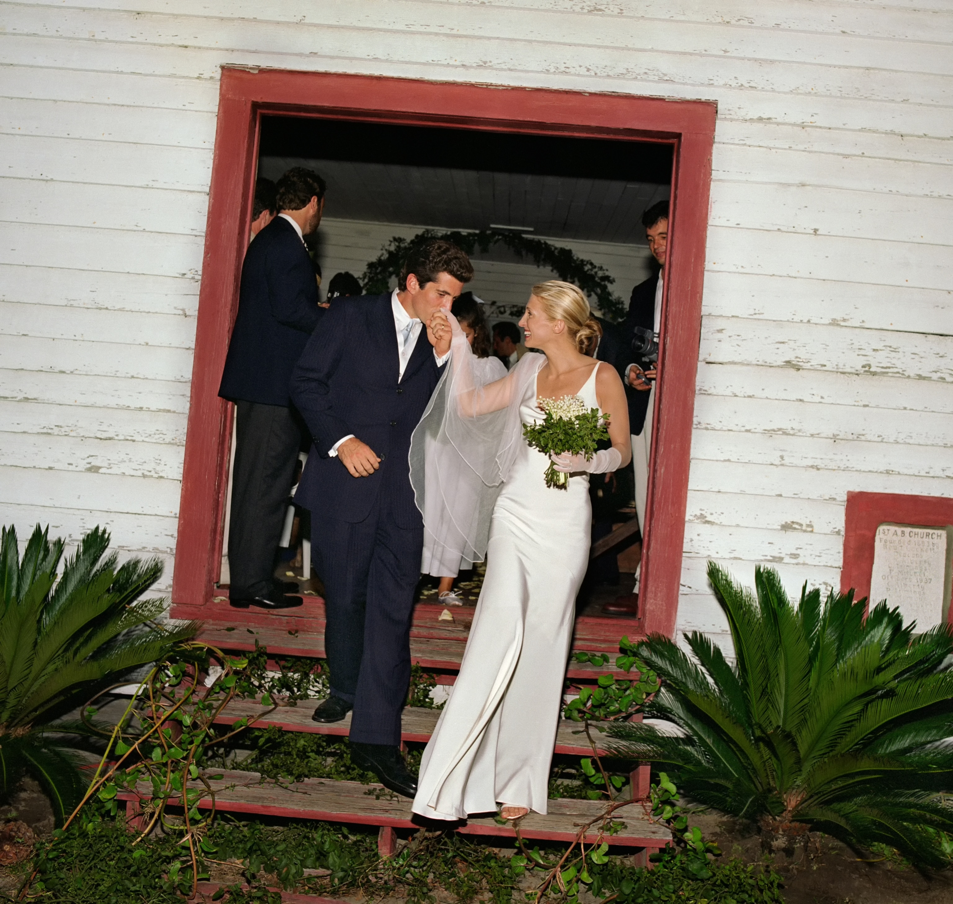JFK Jr. kisses Carolyn Bessette's hand as they walk out of the chapel at their wedding