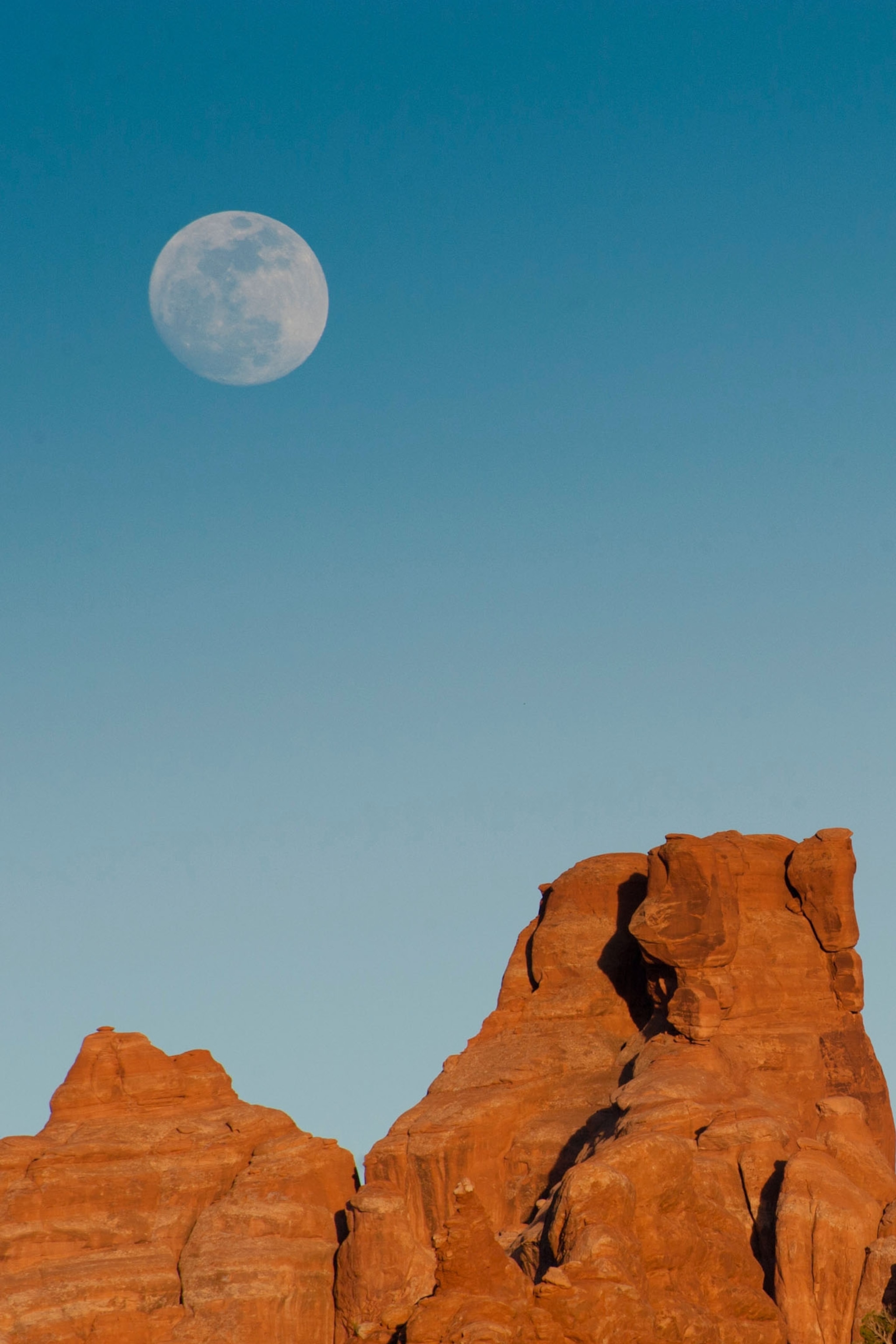 A large rock stands in front of a moon