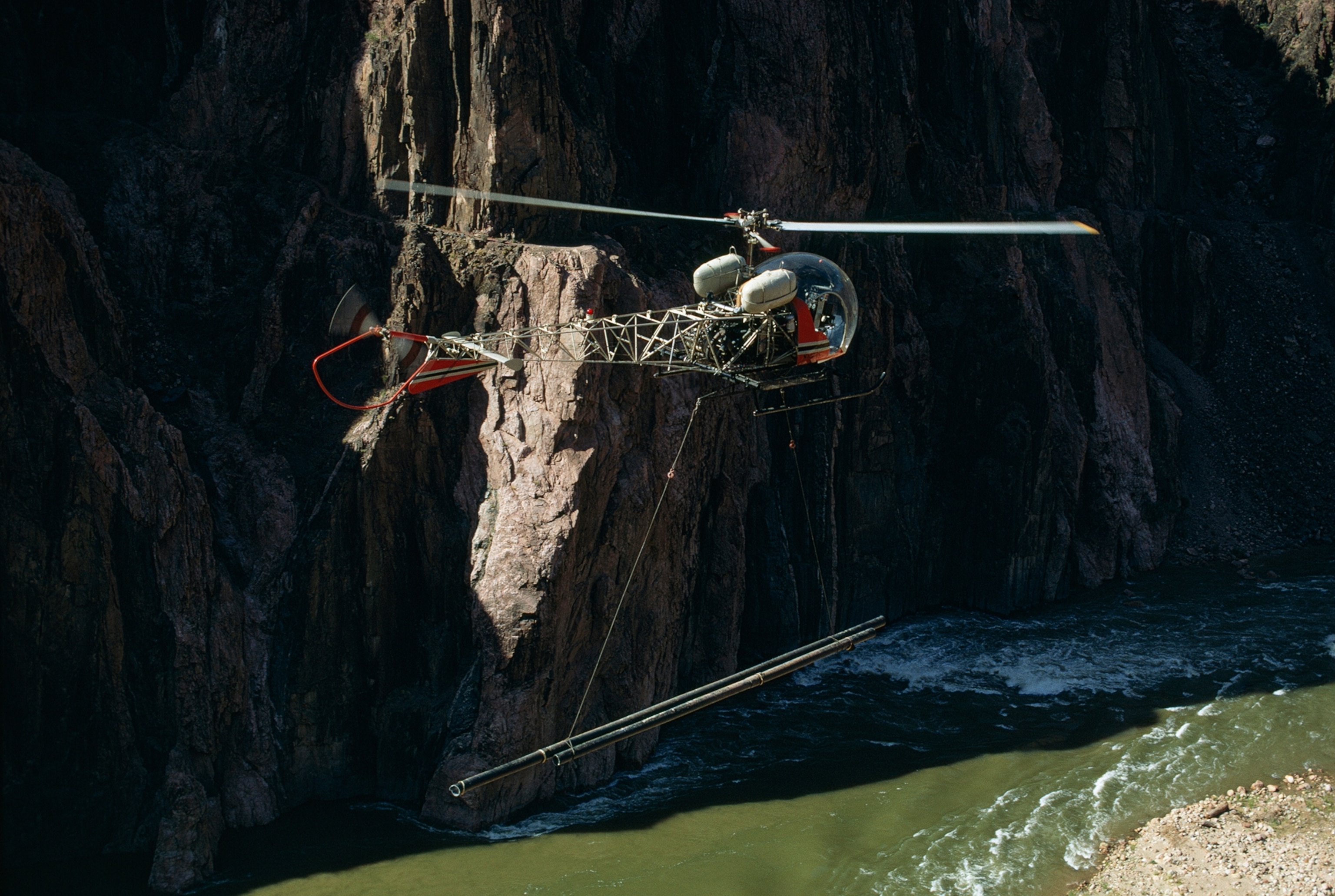 Helicopter carries damaged pipeline washed out by freak downpour.