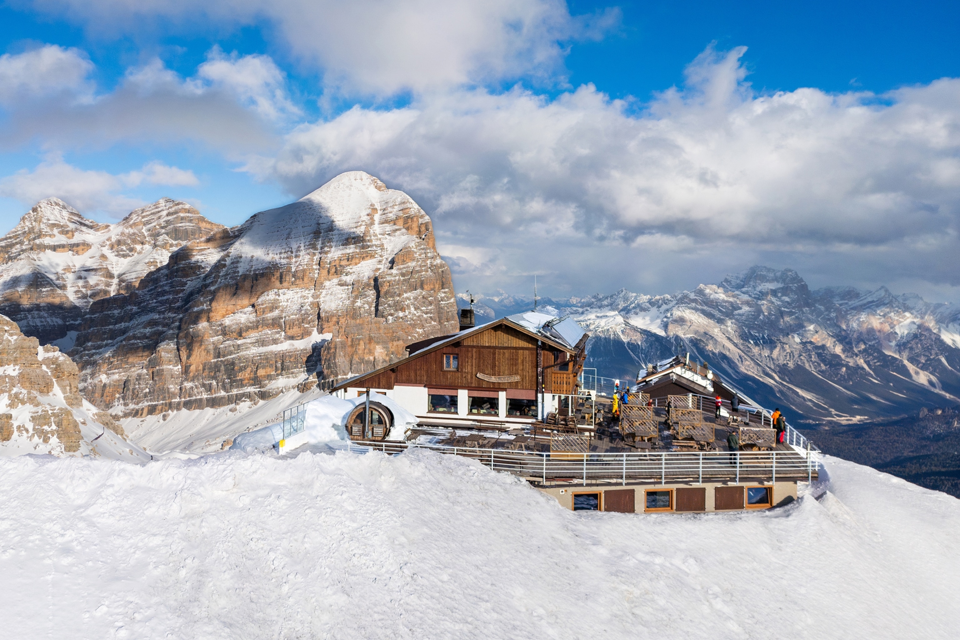 A wooden hut on the peak of a snowy mountain with a terrace overlooking the valley.