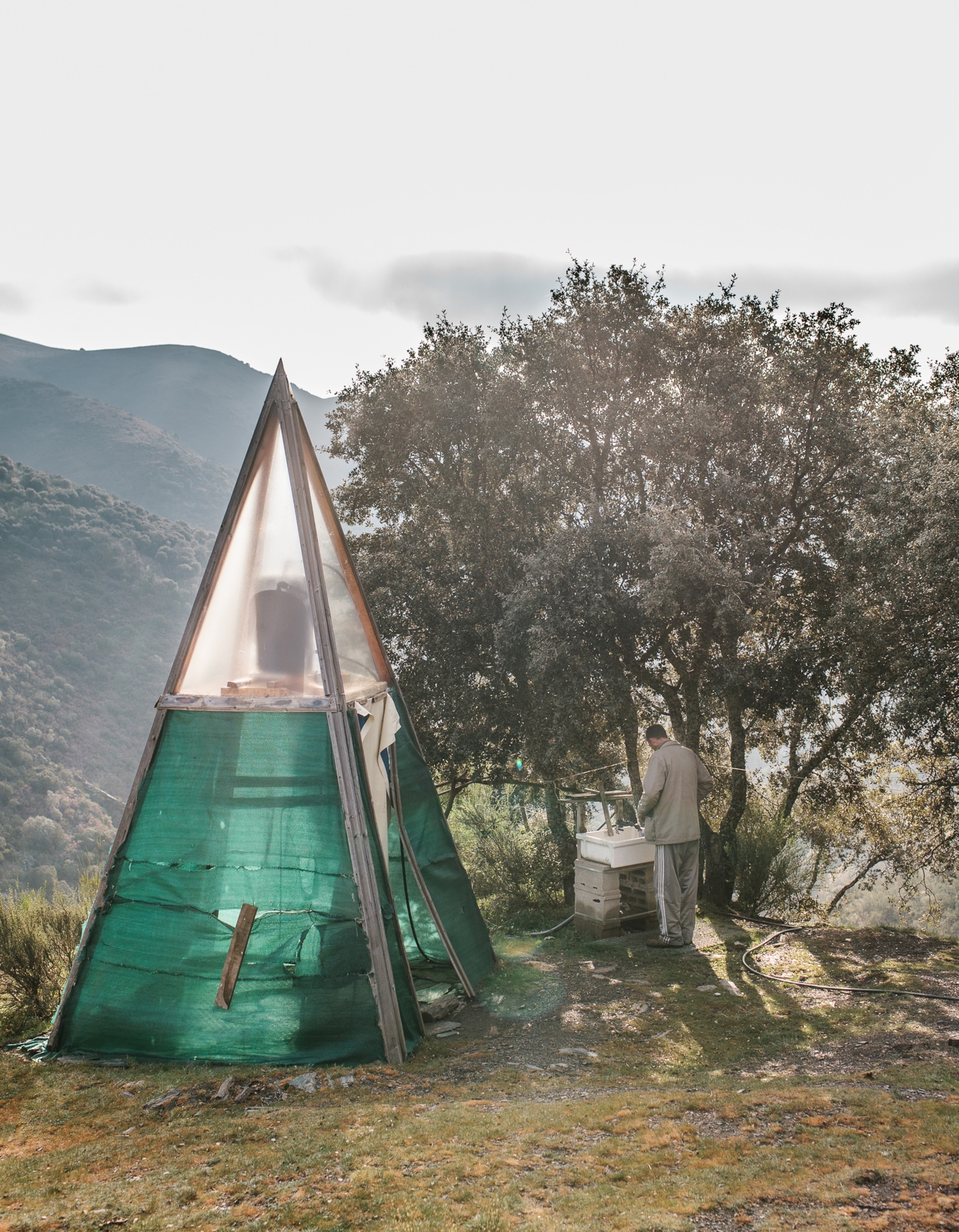 a man standing next to a green teepee prepares for a shower using solar-heated water in the mountains of northwest Spain