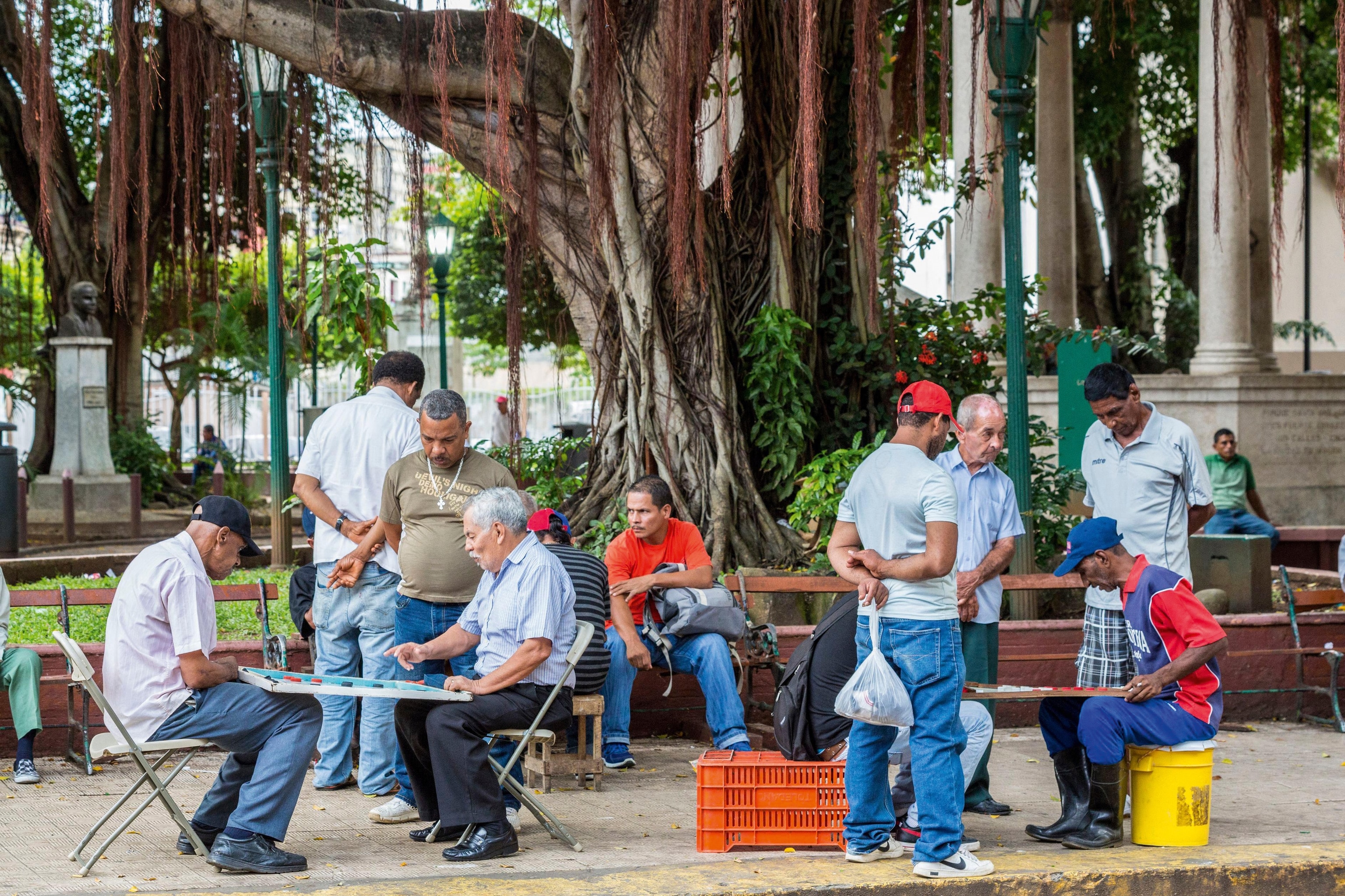 Eight people outdoors chatting and playing domino games