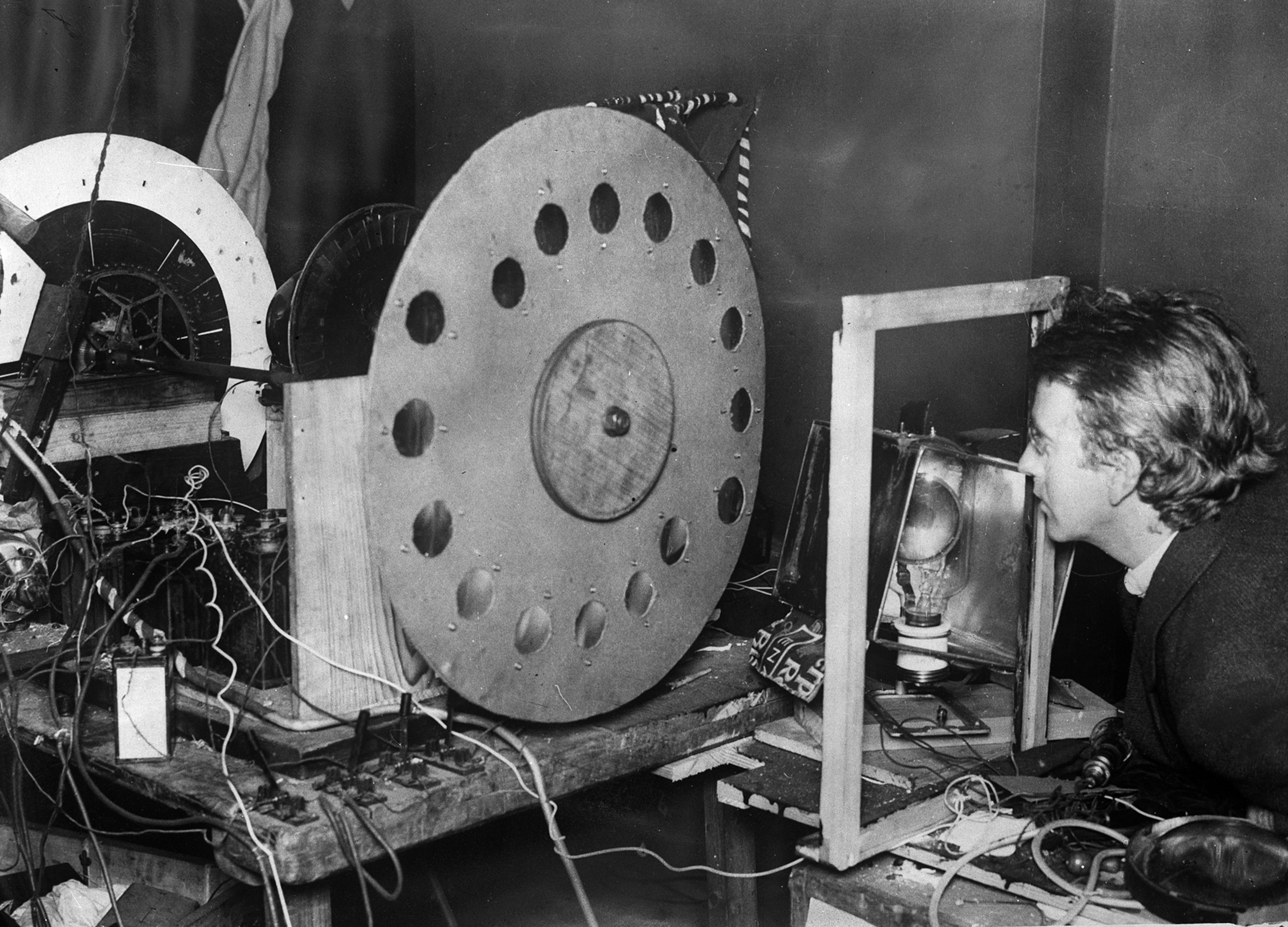 Black and white historical photo of a man peering into a large mechanical device