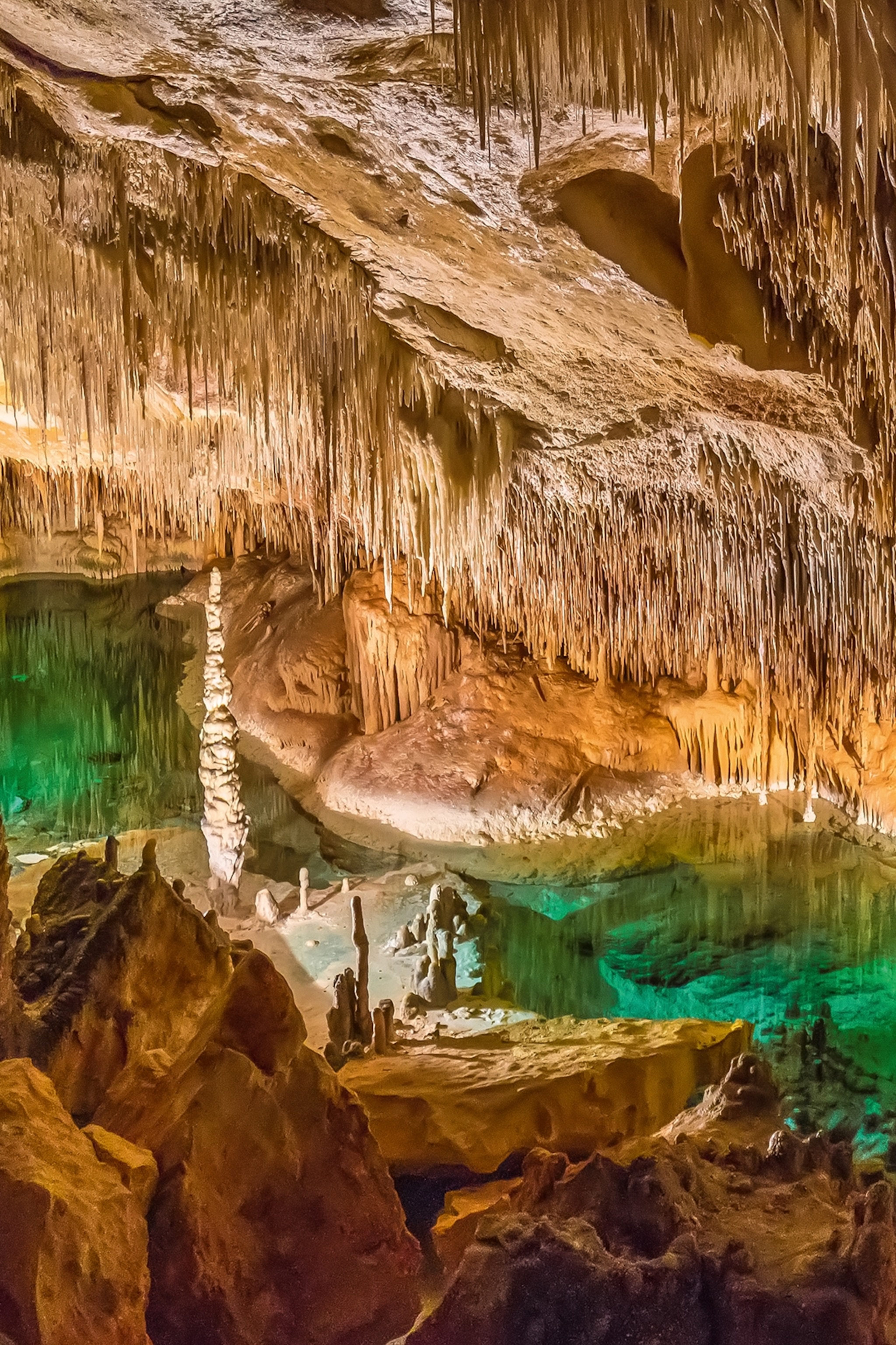 The interior of a lake with an emerald-clear lake and rock formations hanging from the ceiling.