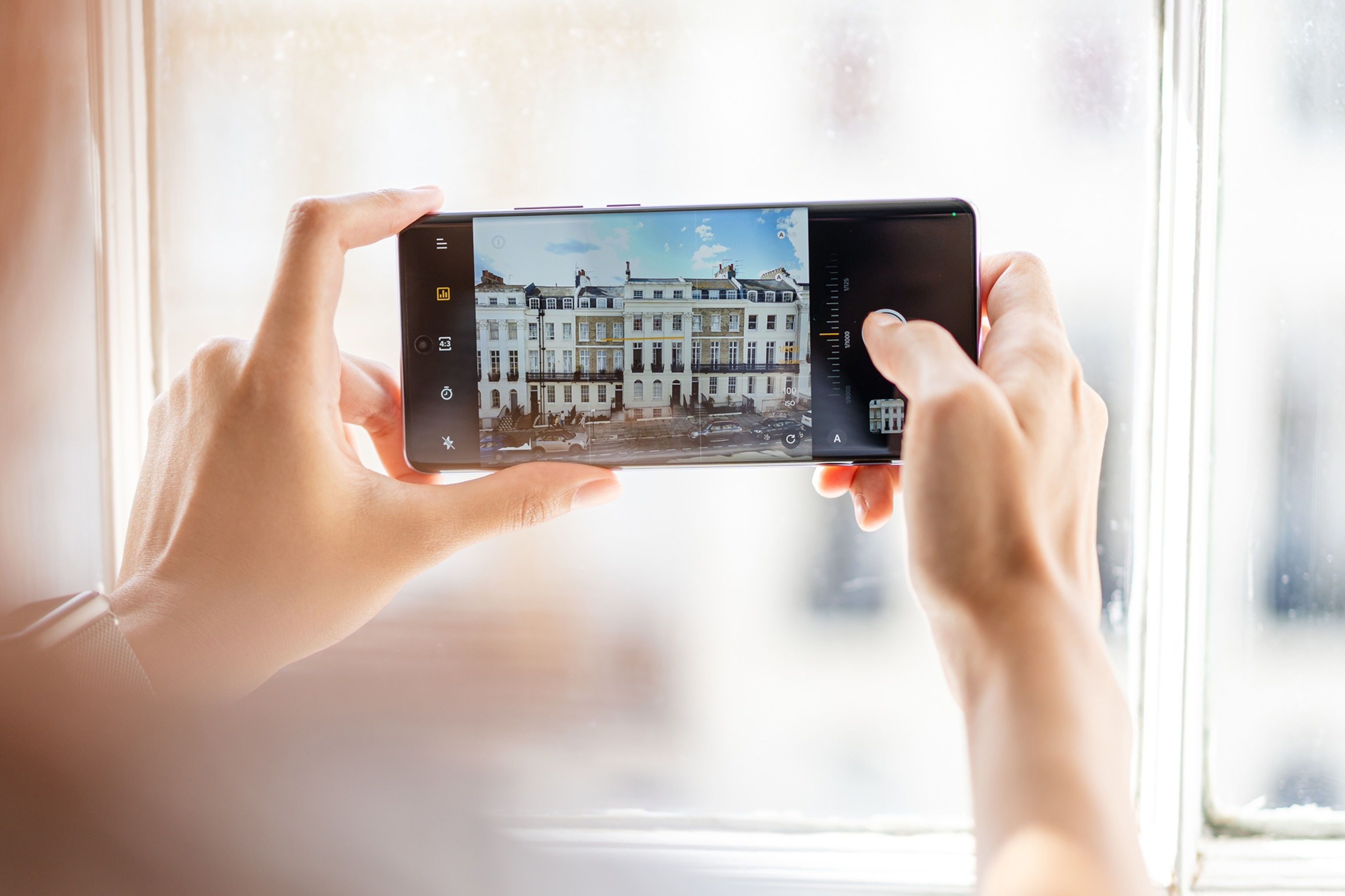 A close-up of a phone being held horizontally, taking a picture of houses in Amsterdam.